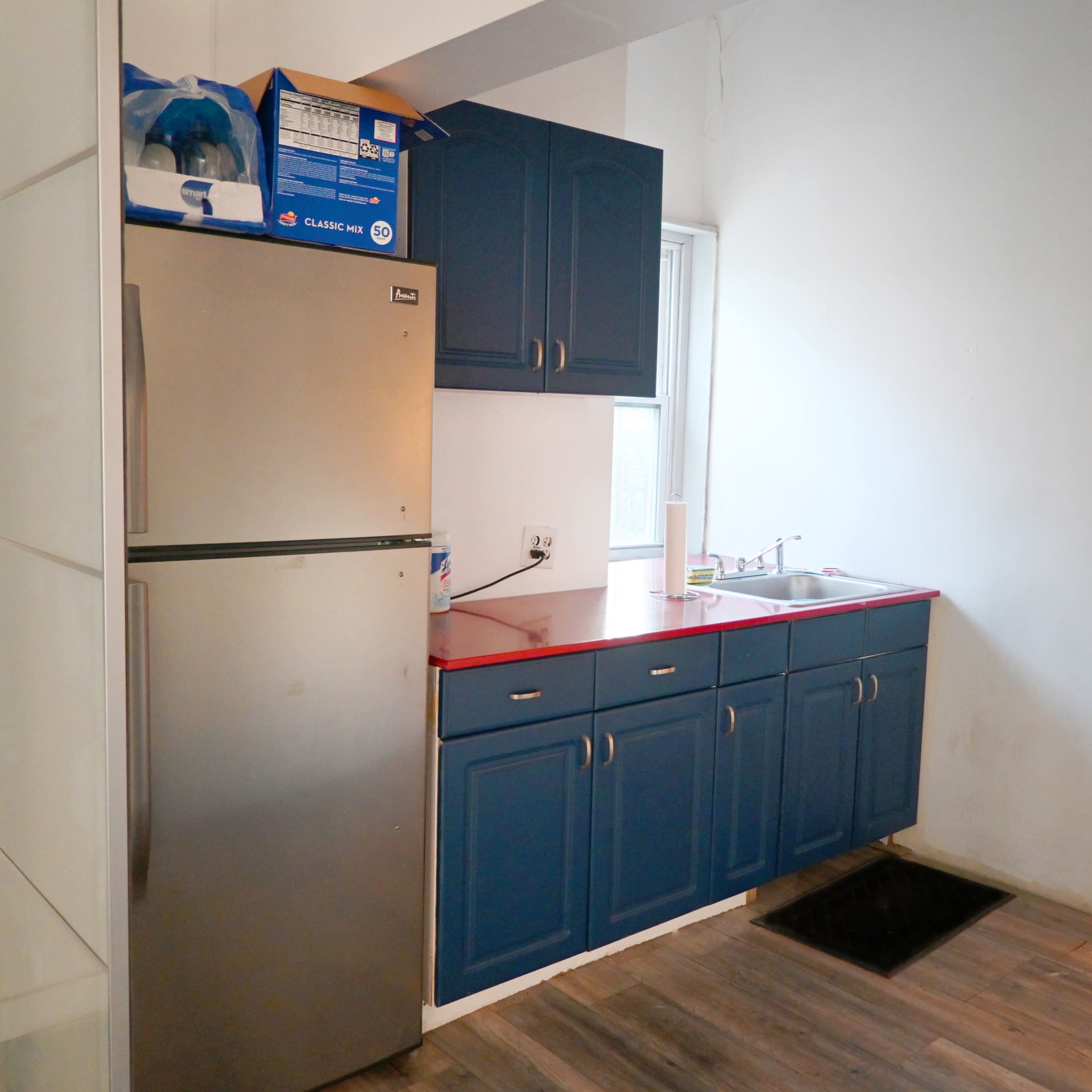 A kitchen area featuring a stainless steel refrigerator, a sink with a countertop, and dark blue cabinets.