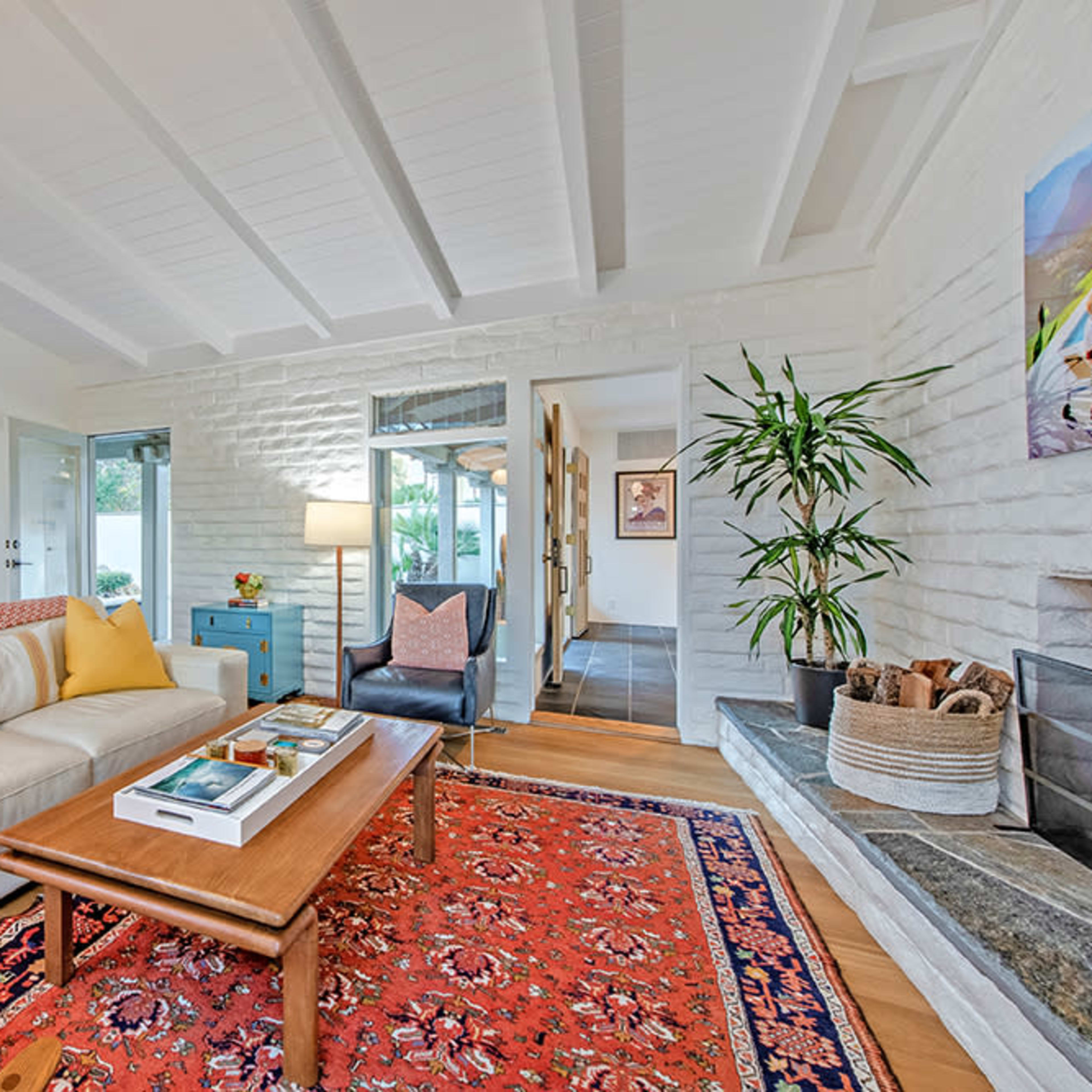 A modern living room featuring a white sofa with yellow pillows, a wooden coffee table, and a decorative rug on the floor.
