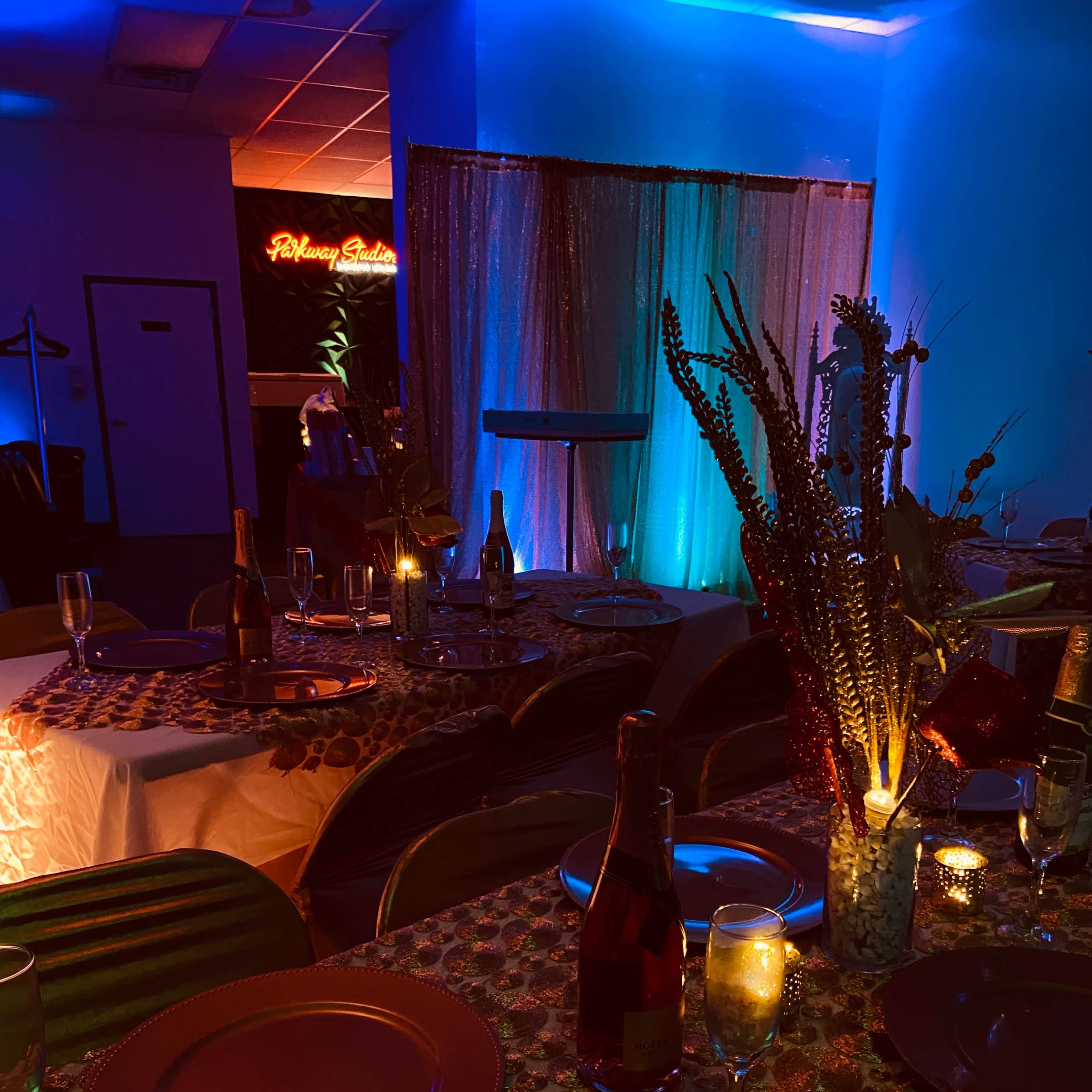 A dining area set with round tables adorned with colorful tablecloths, surrounded by soft blue and warm lighting, creating an inviting atmosphere for guests.