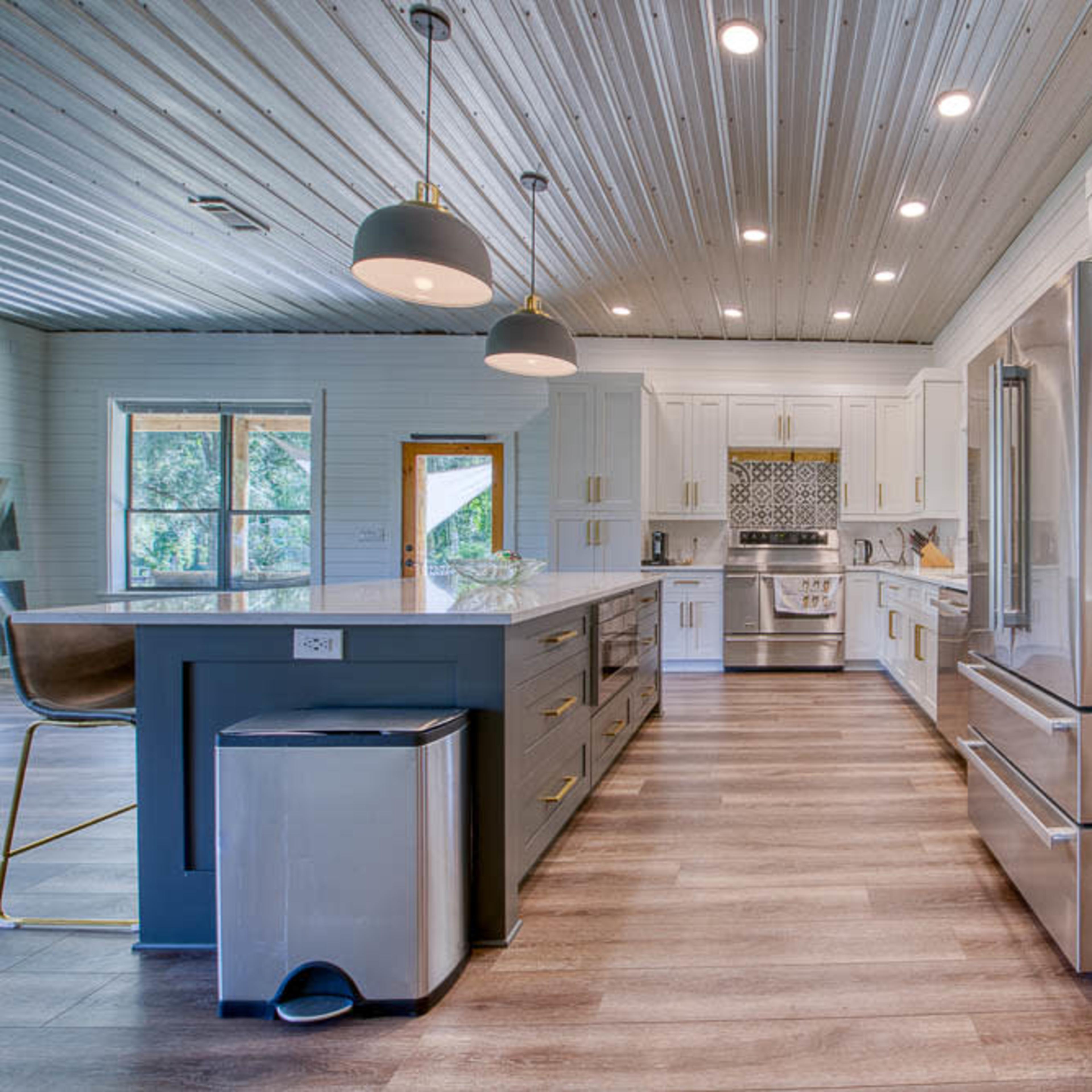 A modern kitchen features a large island, stainless steel appliances, and white cabinetry with natural light streaming through the windows.