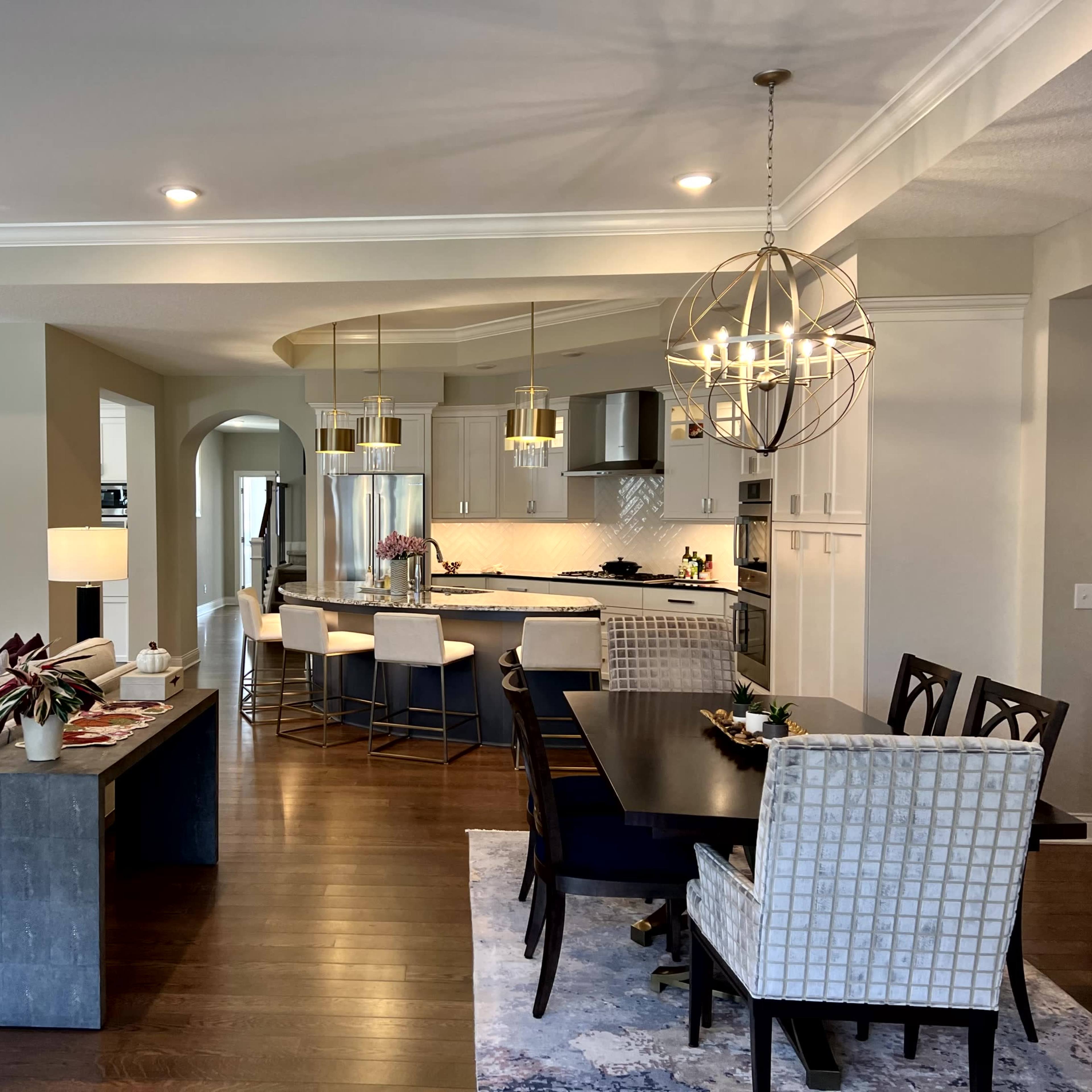 A modern open-concept kitchen and dining area with a large dining table, bar seating, and contemporary lighting fixtures.