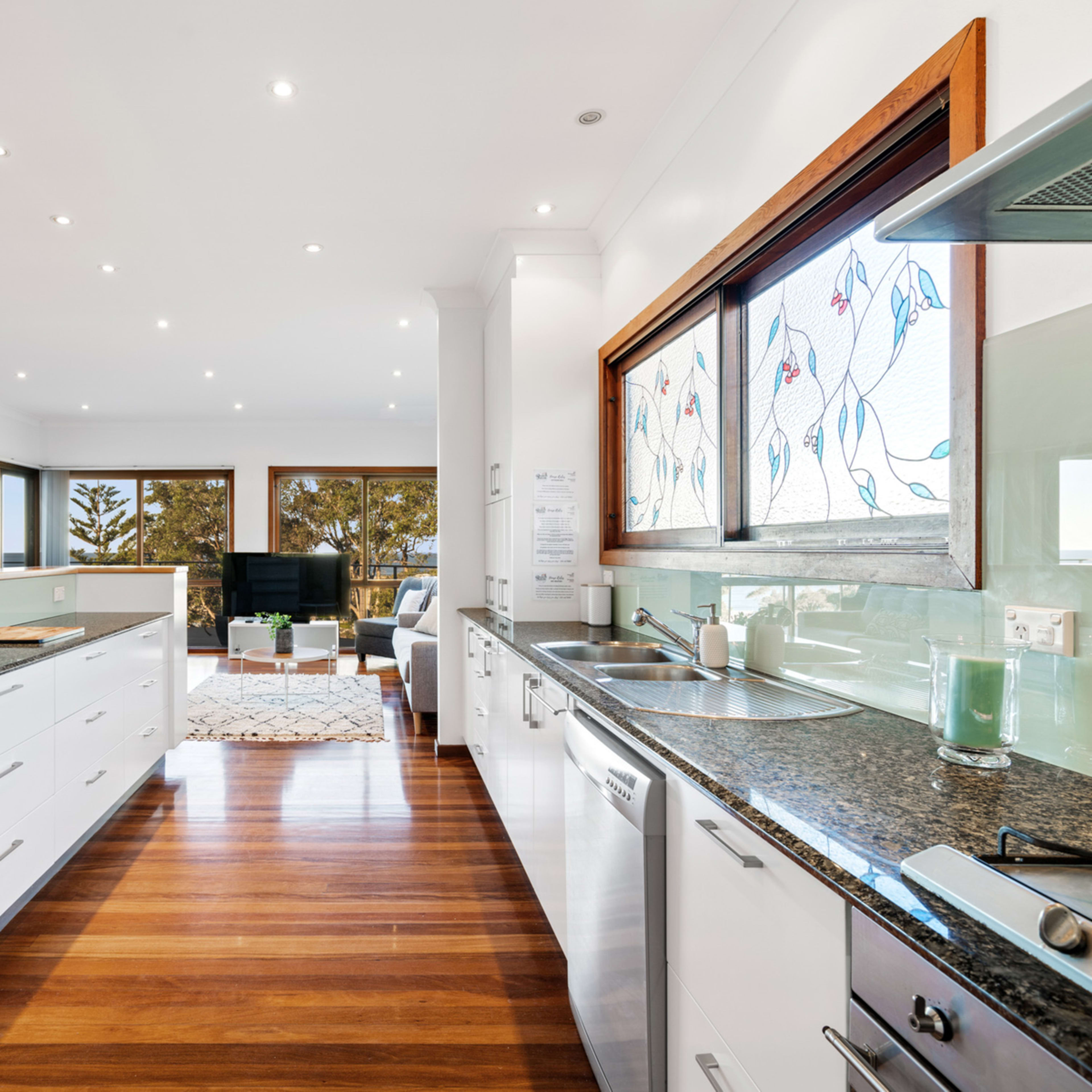 A modern kitchen with white cabinetry, a granite countertop, and large windows overlooking a bright living area.