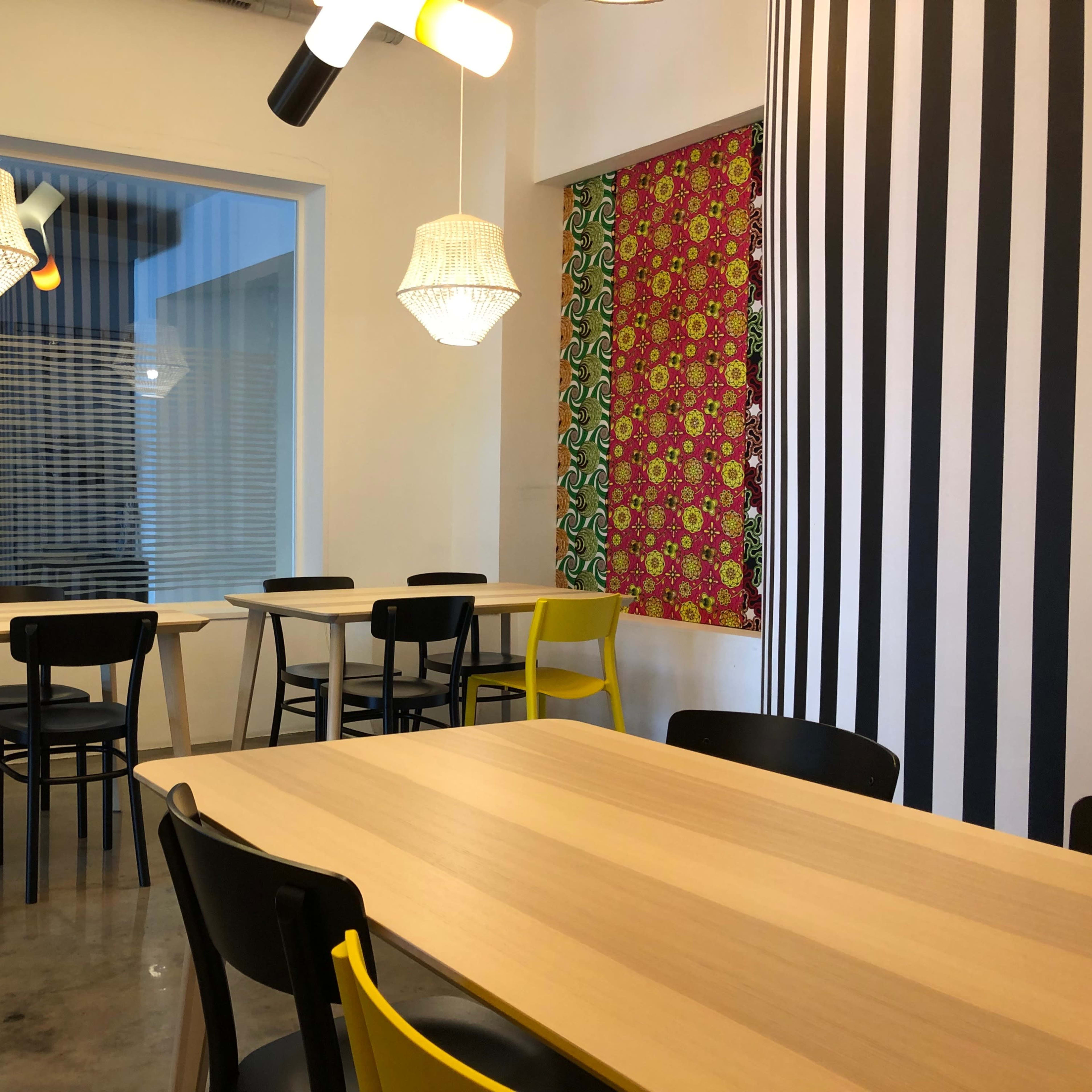 A modern dining area with wooden tables and a mix of yellow and black chairs, accompanied by decorative wall elements and pendant lighting.