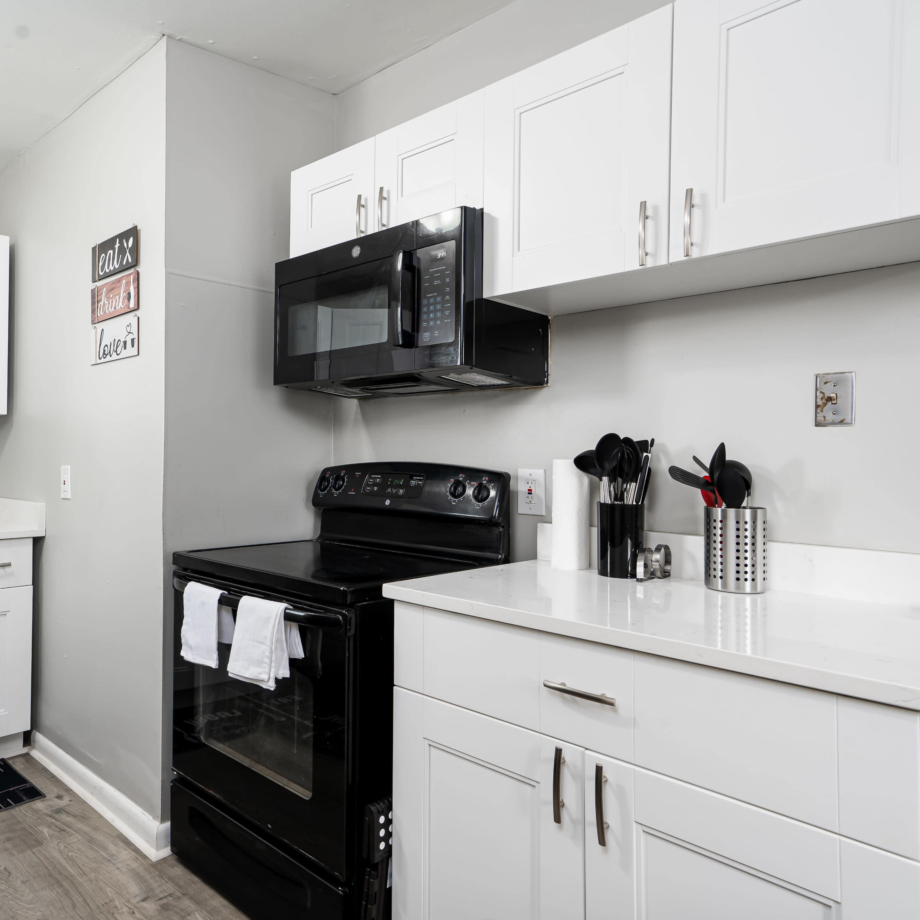 A modern kitchen with white cabinetry, a black stove and microwave, and a gray wall.