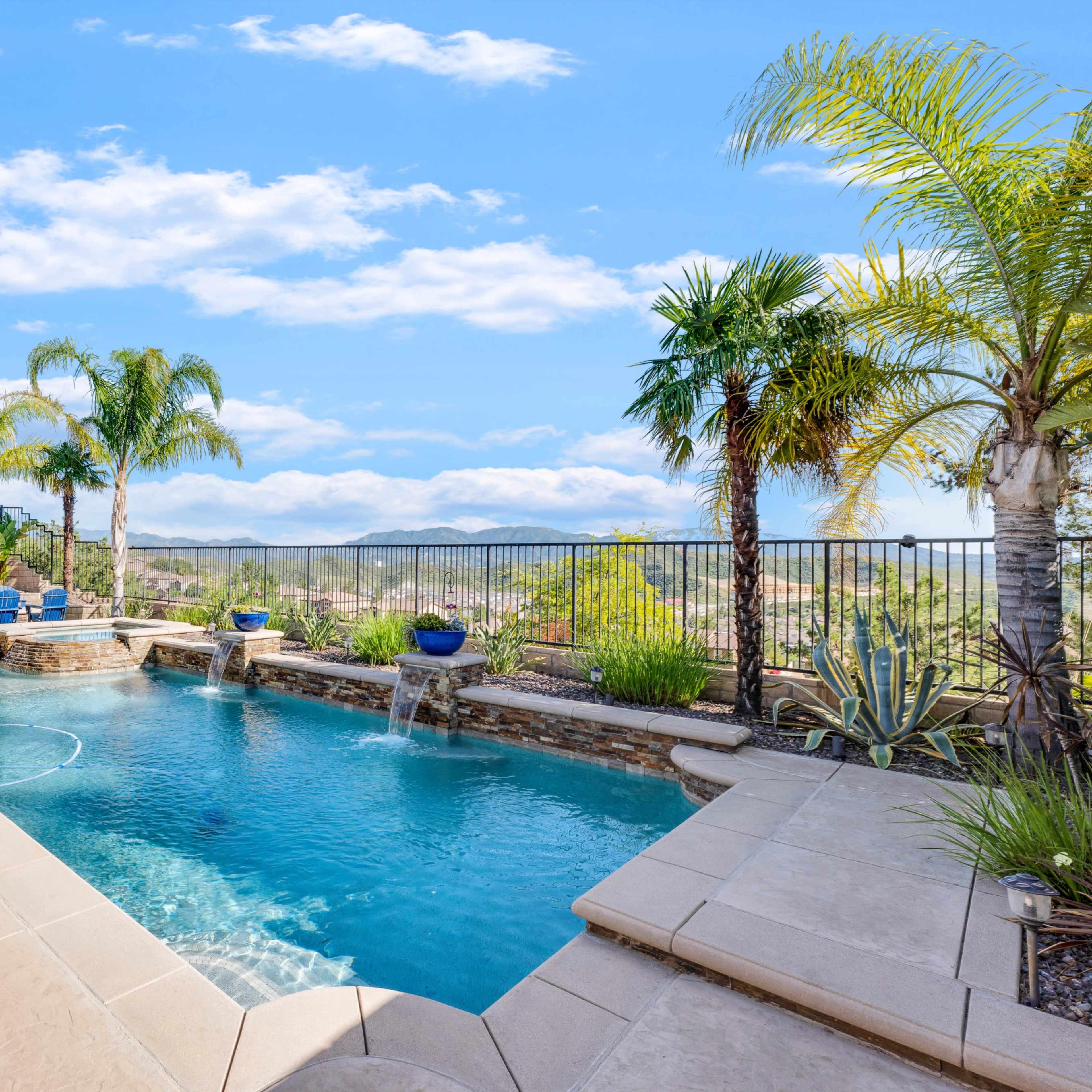 A swimming pool surrounded by palm trees and landscaped greenery, with a mountain view in the background.