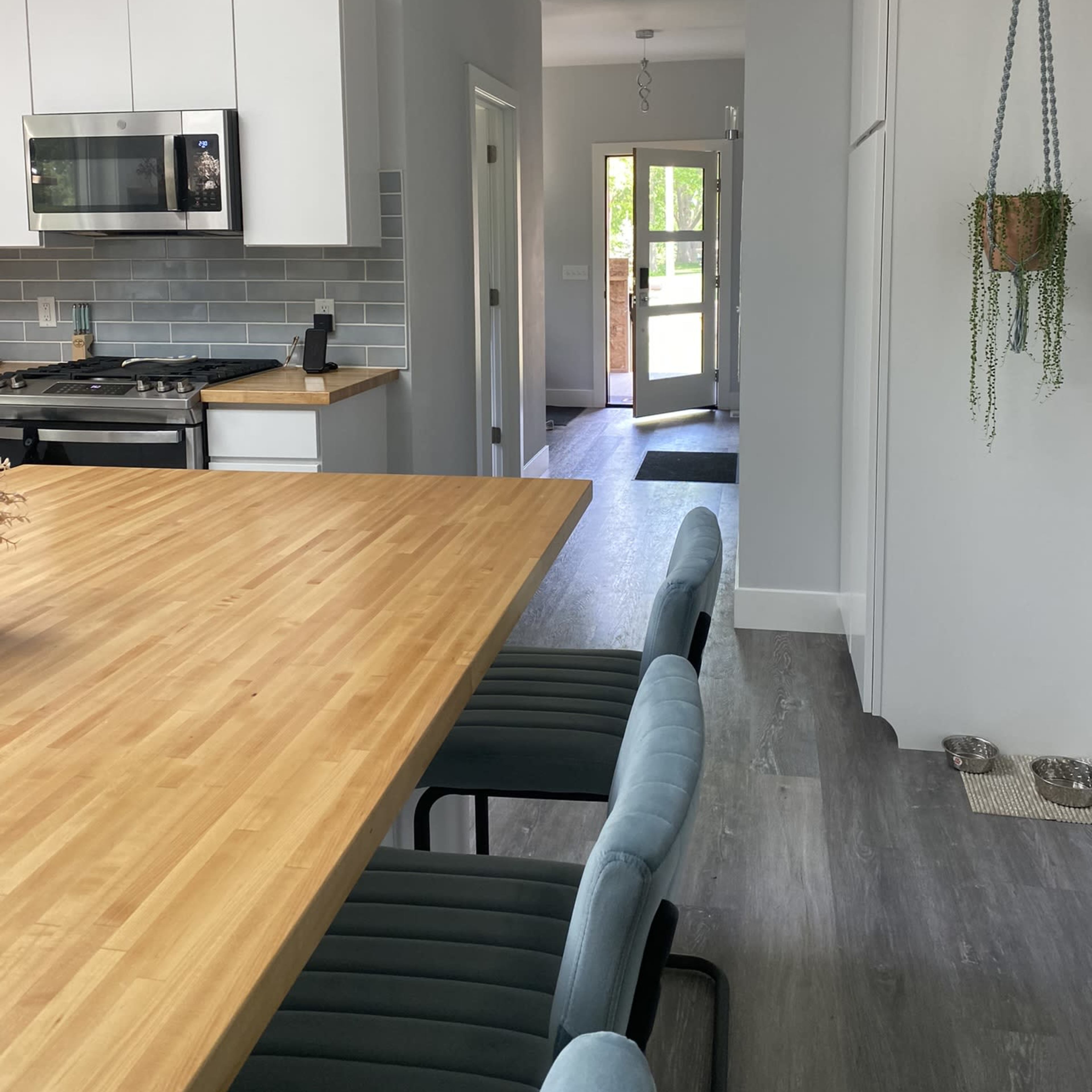 A modern kitchen and dining area with a large wooden table, light blue chairs, stainless steel appliances, and a doorway leading to an outside entrance.