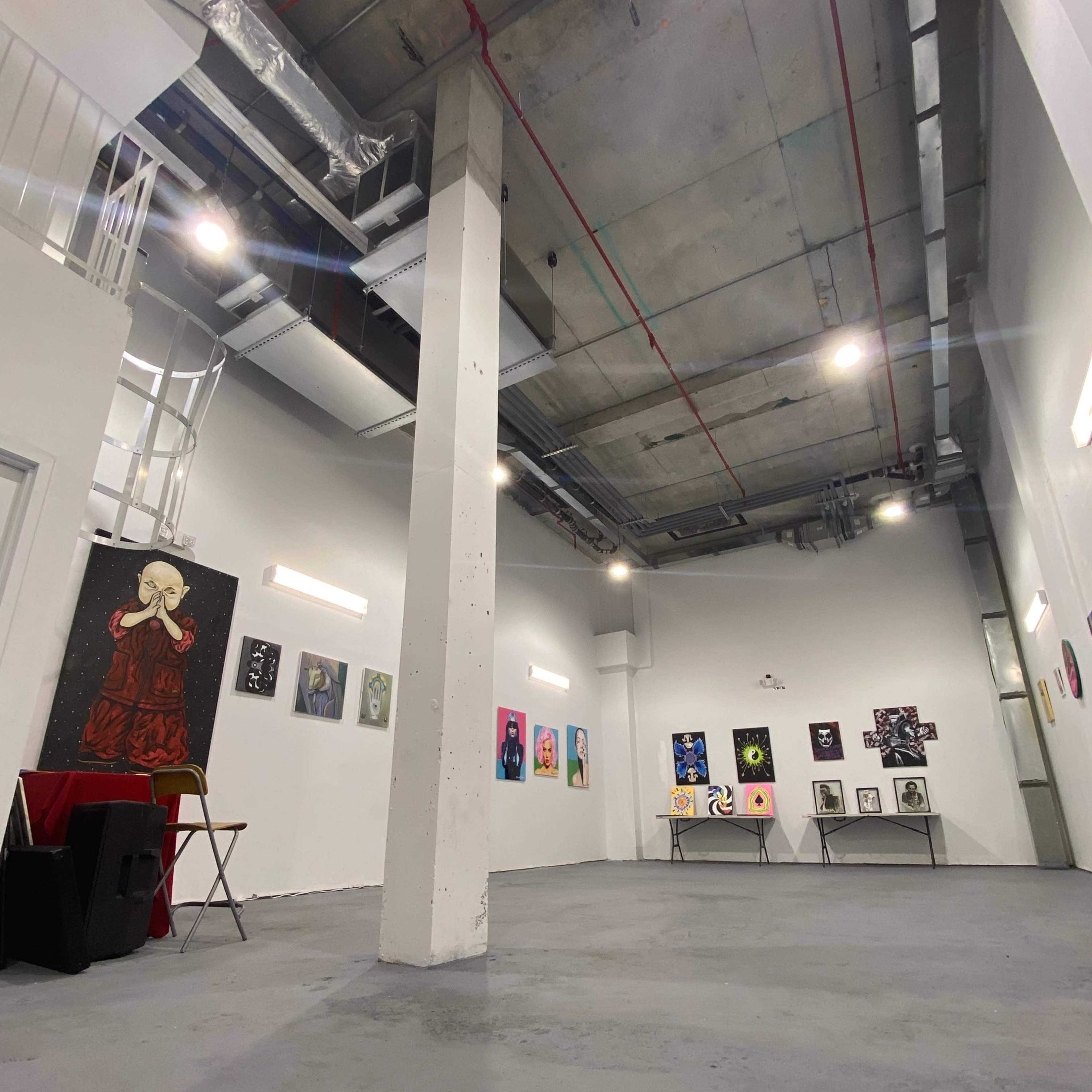 An interior gallery space with a polished concrete floor, featuring various artworks displayed on white walls under bright overhead lighting.