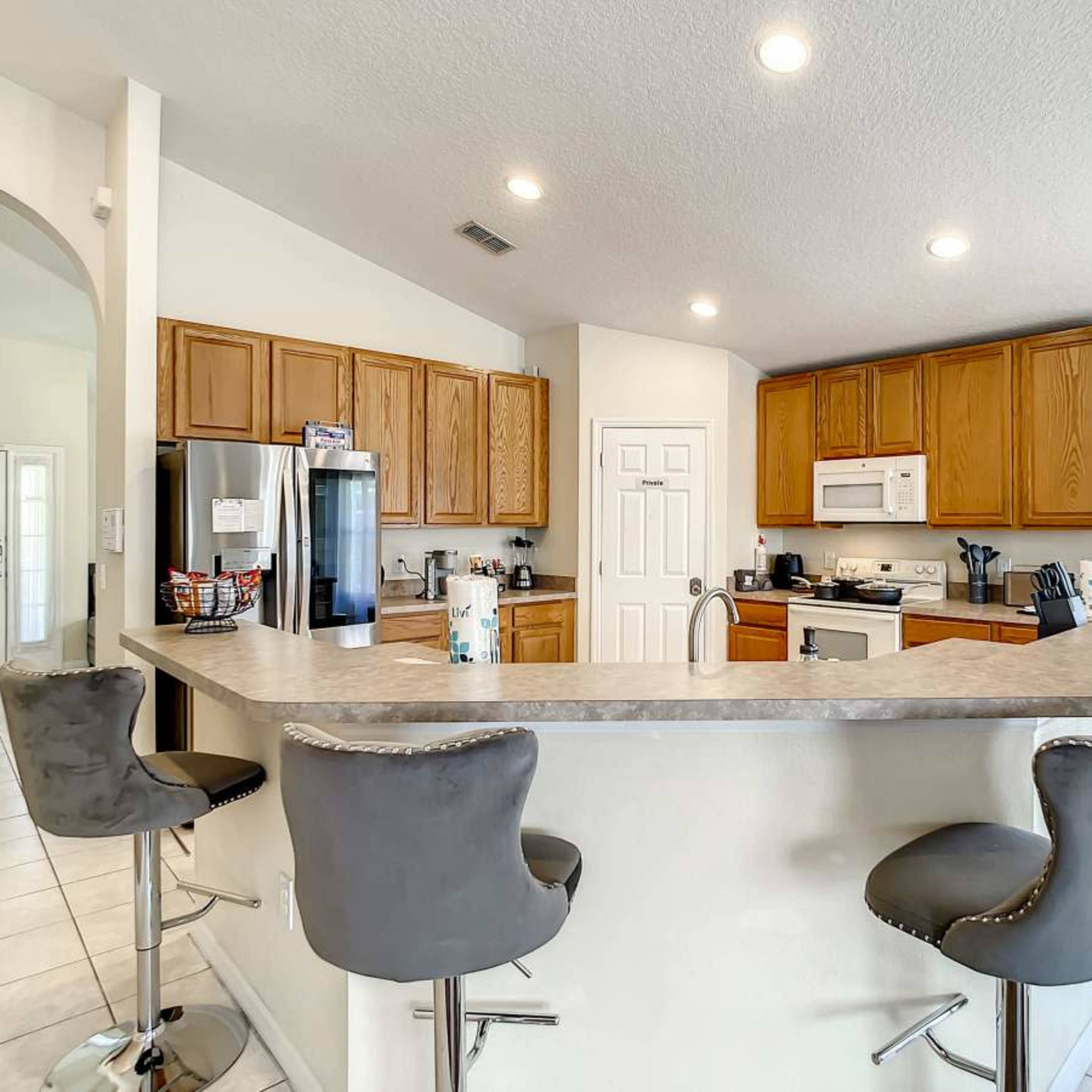 A kitchen features wooden cabinets, a central island with bar seating, and appliances including a refrigerator and oven.