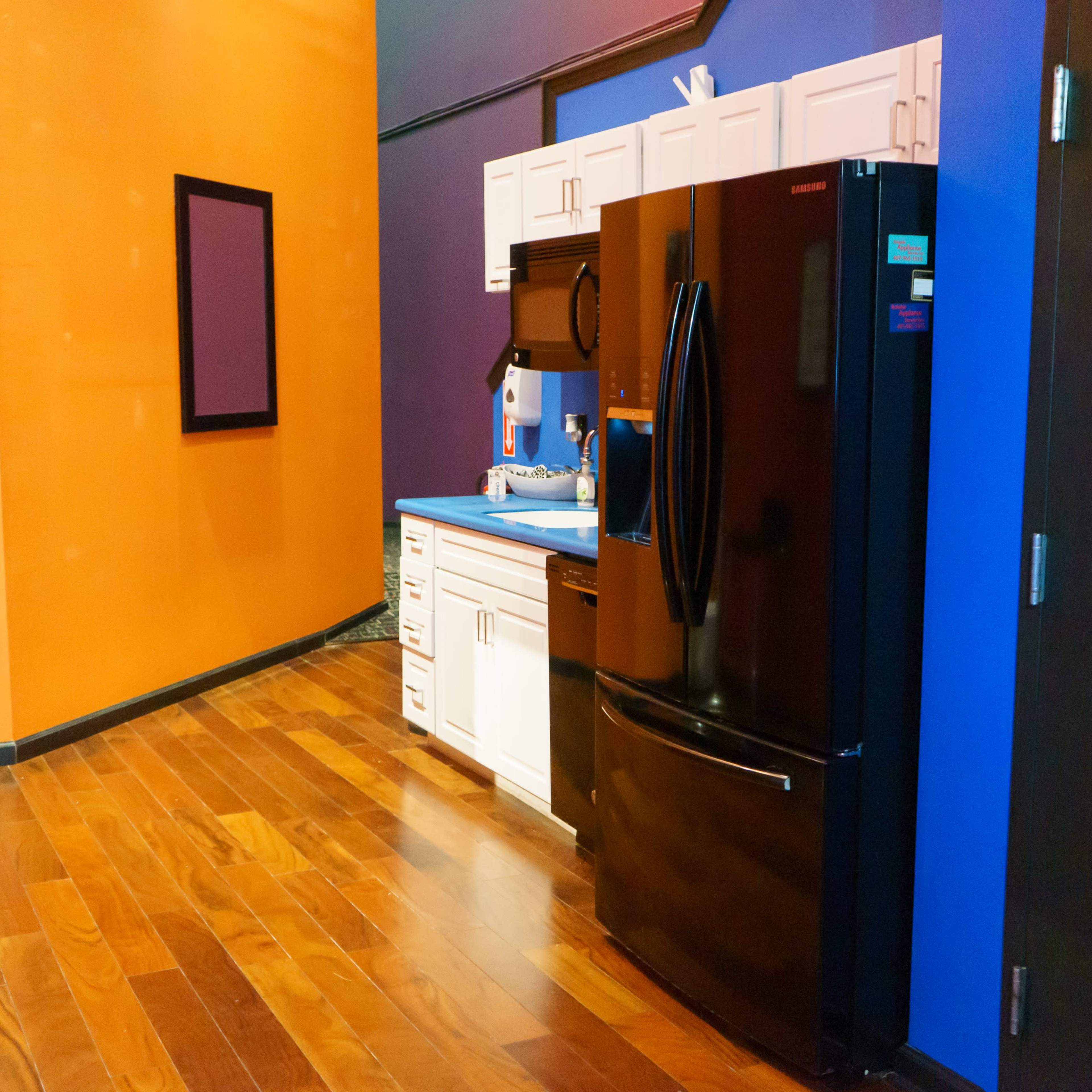 A modern kitchenette featuring a black refrigerator, white cabinetry, and an orange and blue wall.