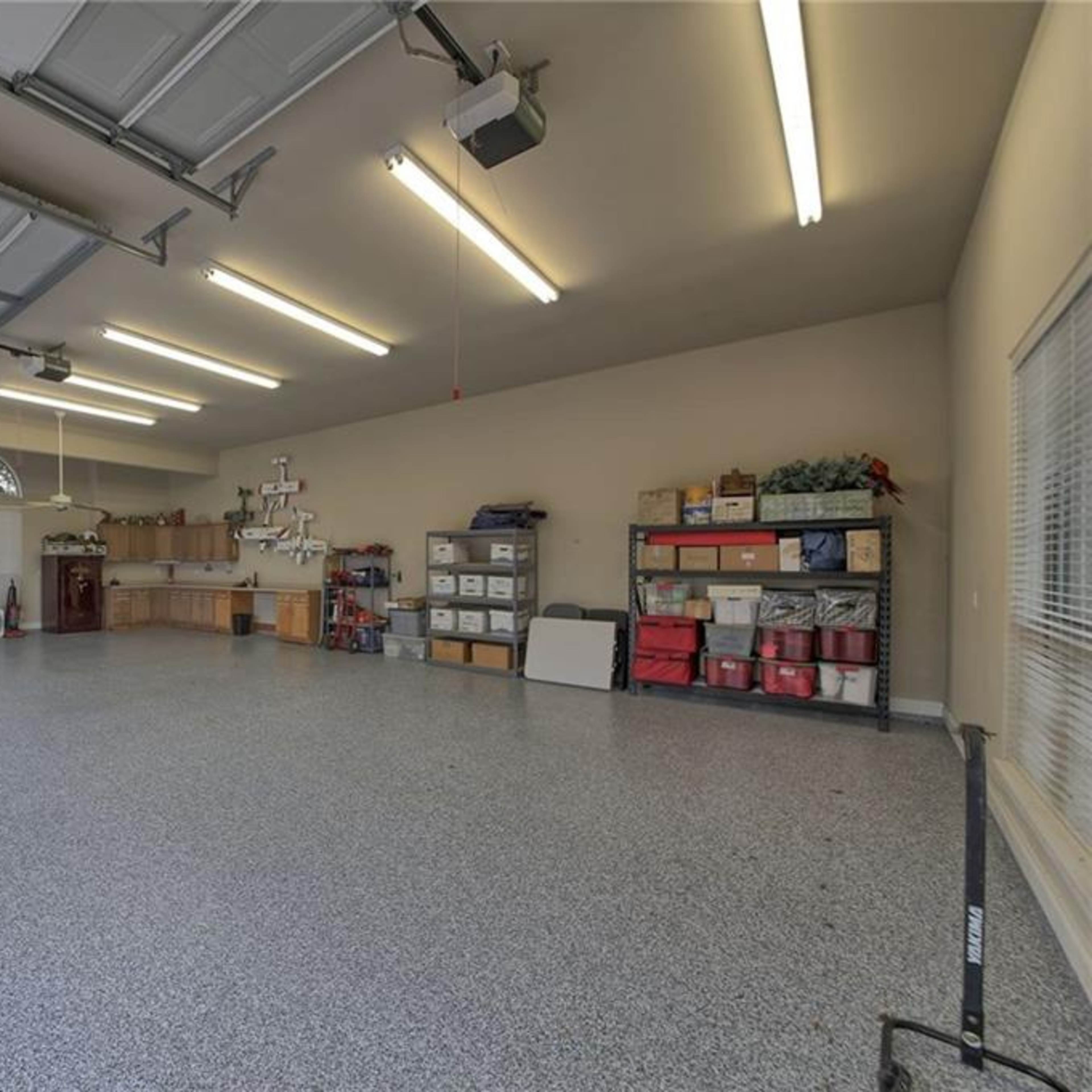 A spacious garage with a smooth, gray floor, overhead lighting, and organized storage shelves along the walls.