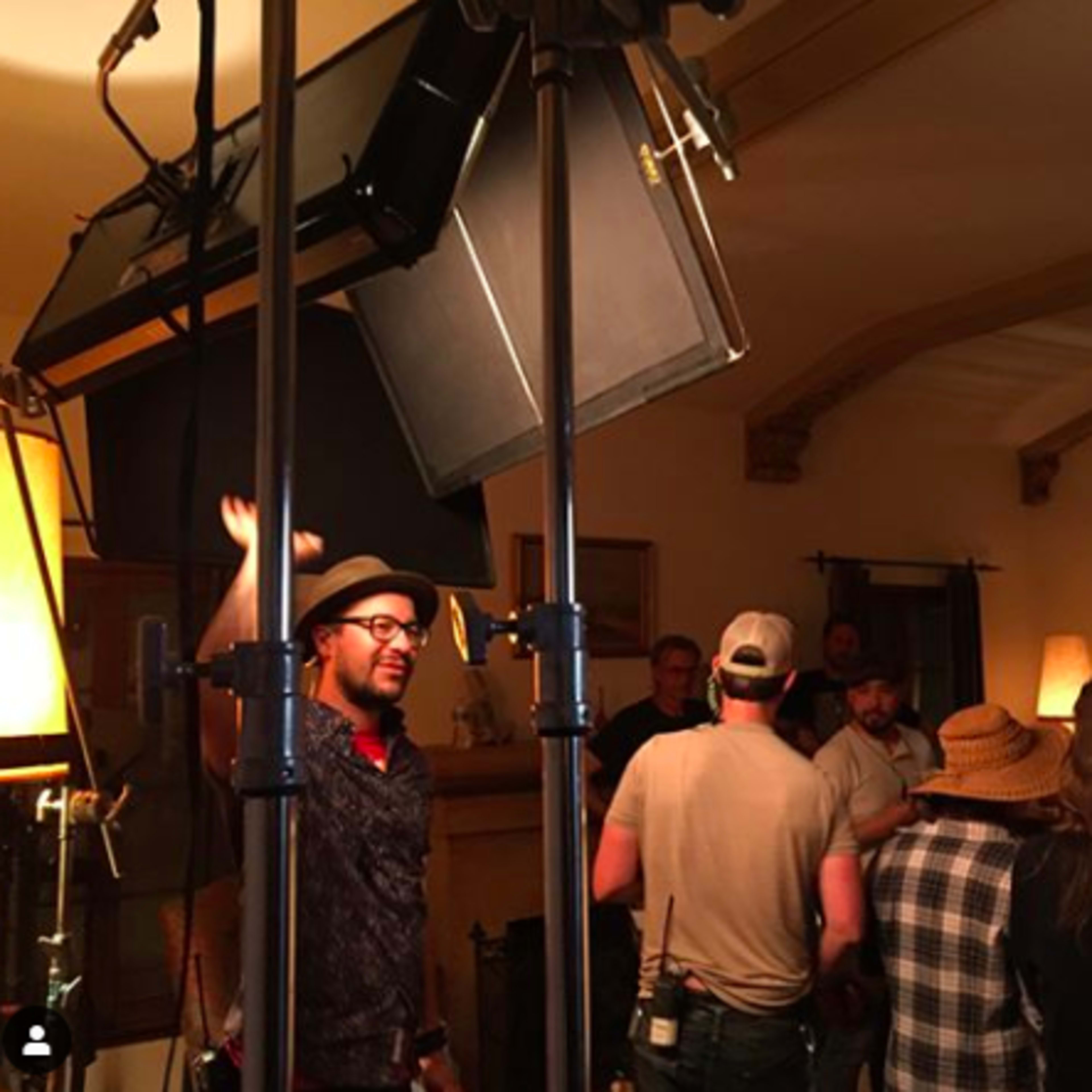 A group of people is gathered in a well-lit room, with film equipment and lights set up for a shoot.