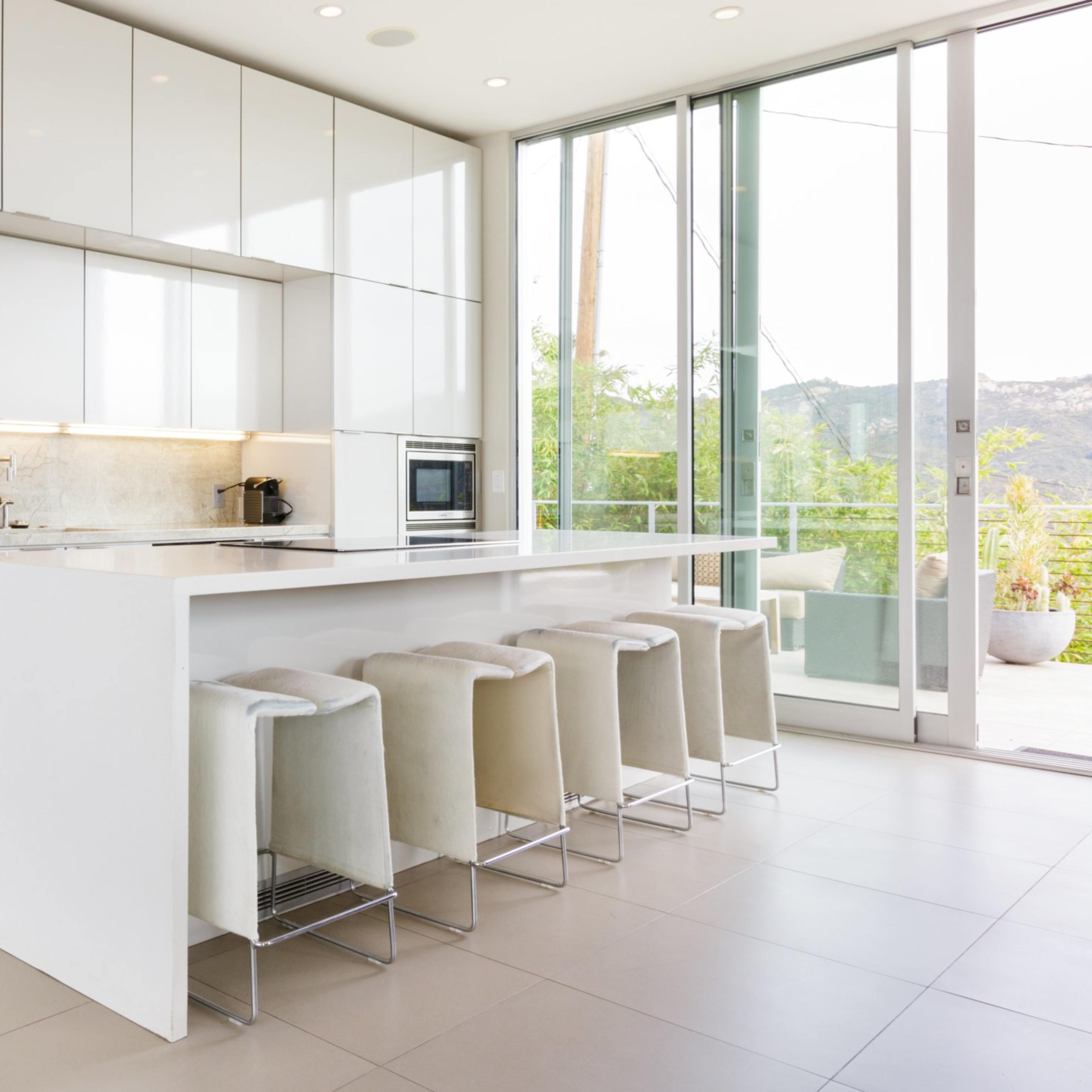 A modern kitchen with white cabinetry, stainless steel appliances, and a long island with six stools.