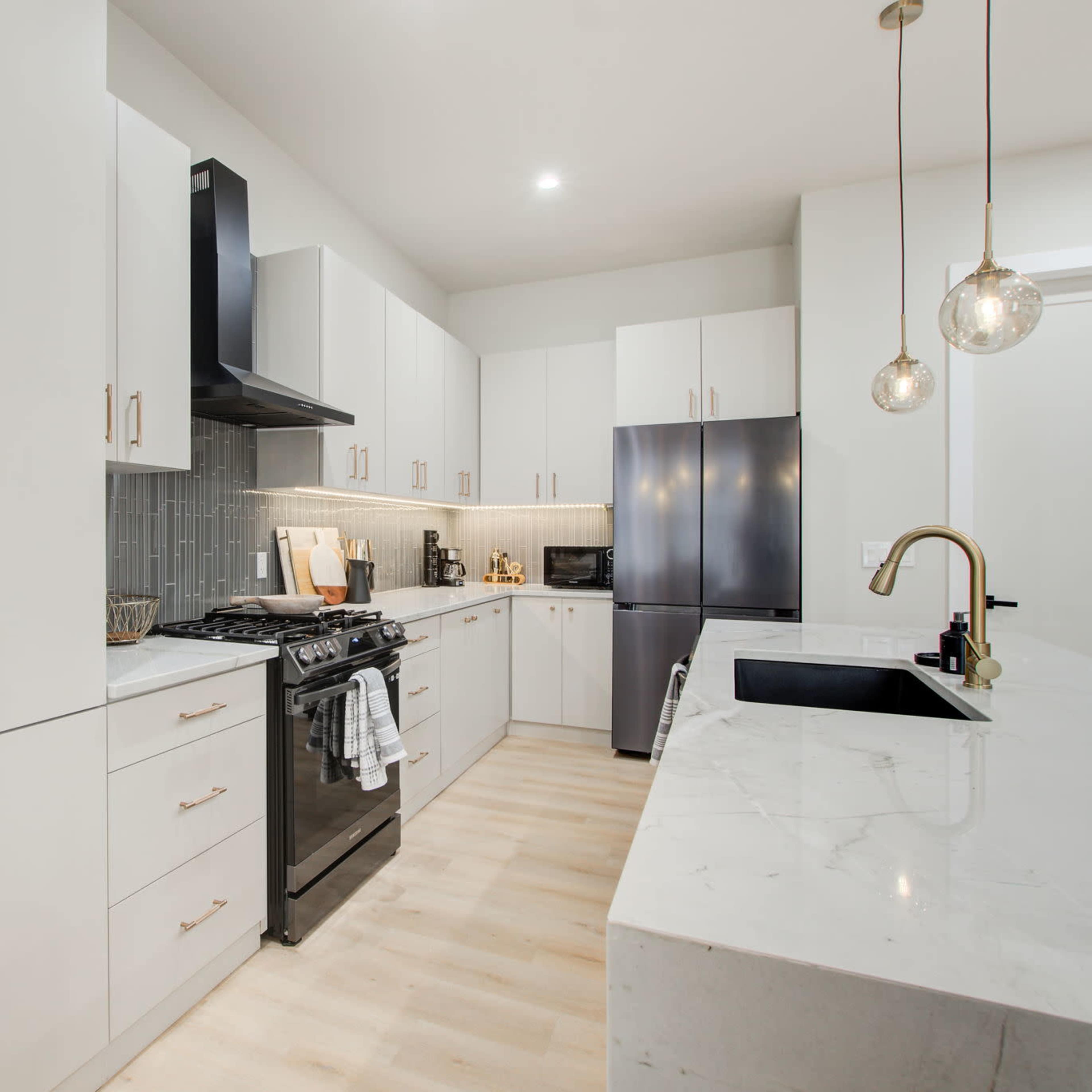 A modern kitchen features white cabinetry, a black stove, and a marble countertop with pendant lights overhead.