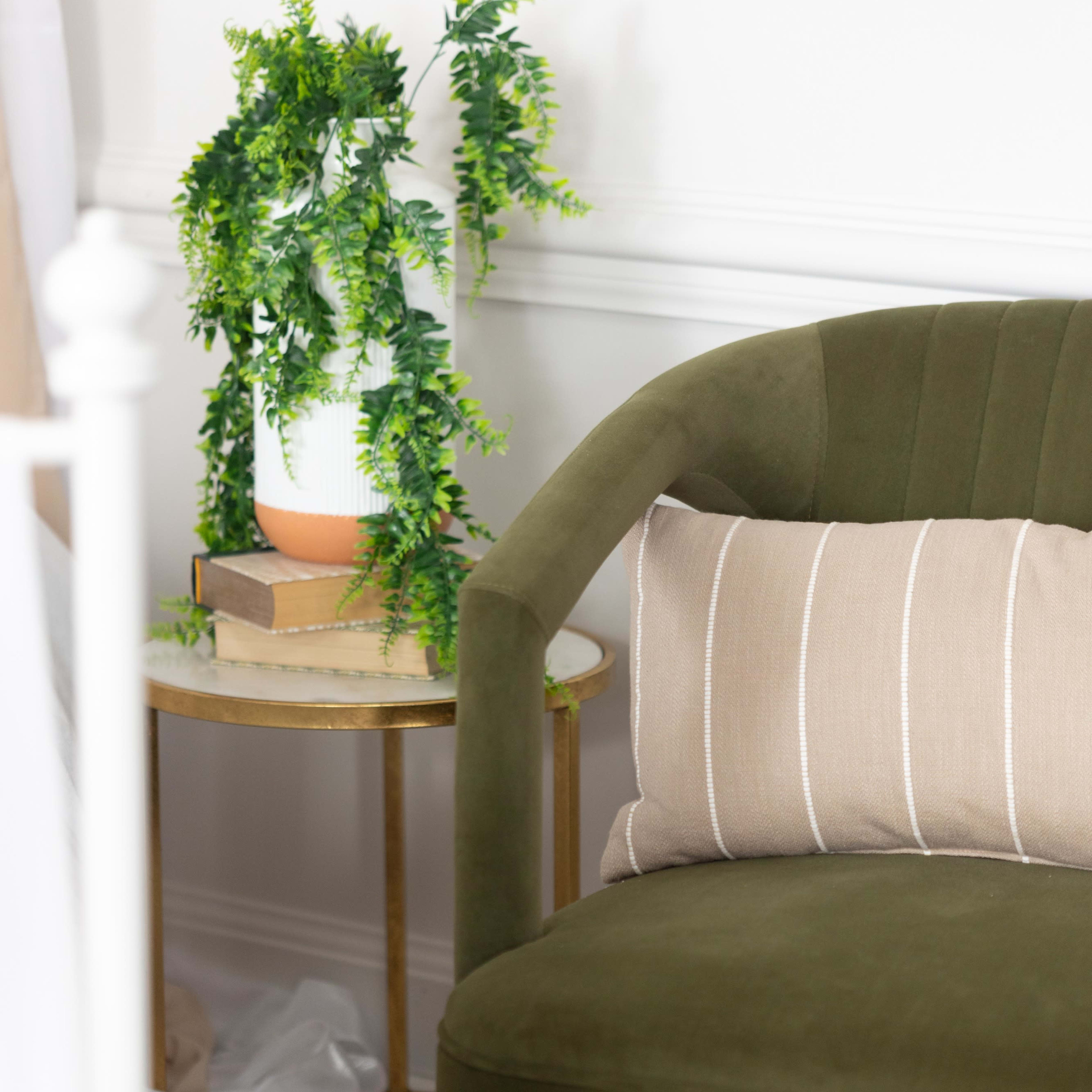 A green chair with a striped pillow is positioned beside a small side table holding a potted plant and a stack of books.
