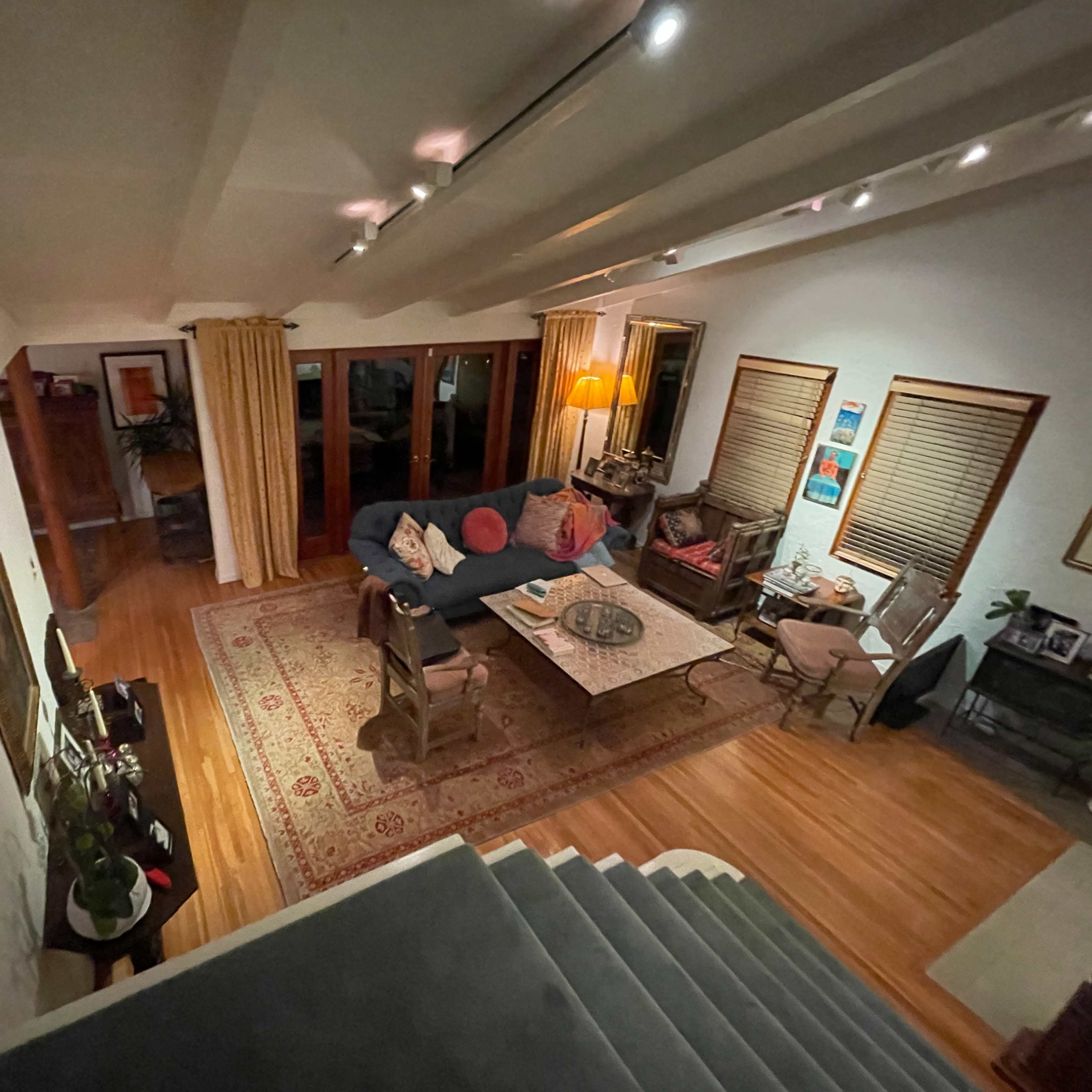 A spacious living room features a blue sofa, a coffee table, and large windows with curtains.