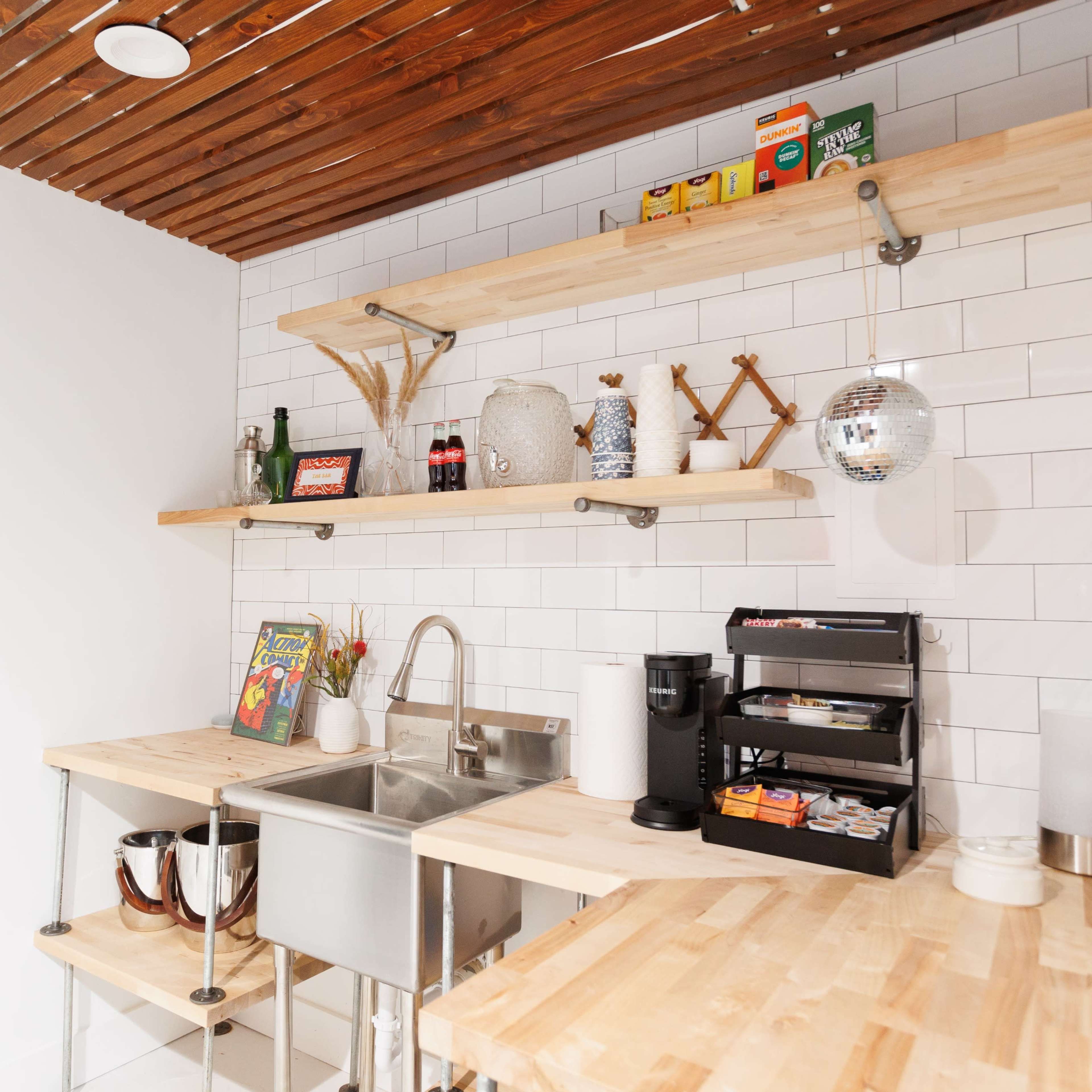 A kitchen area with wooden shelves, a stainless steel sink, and a coffee station with various supplies and a small disco ball.
