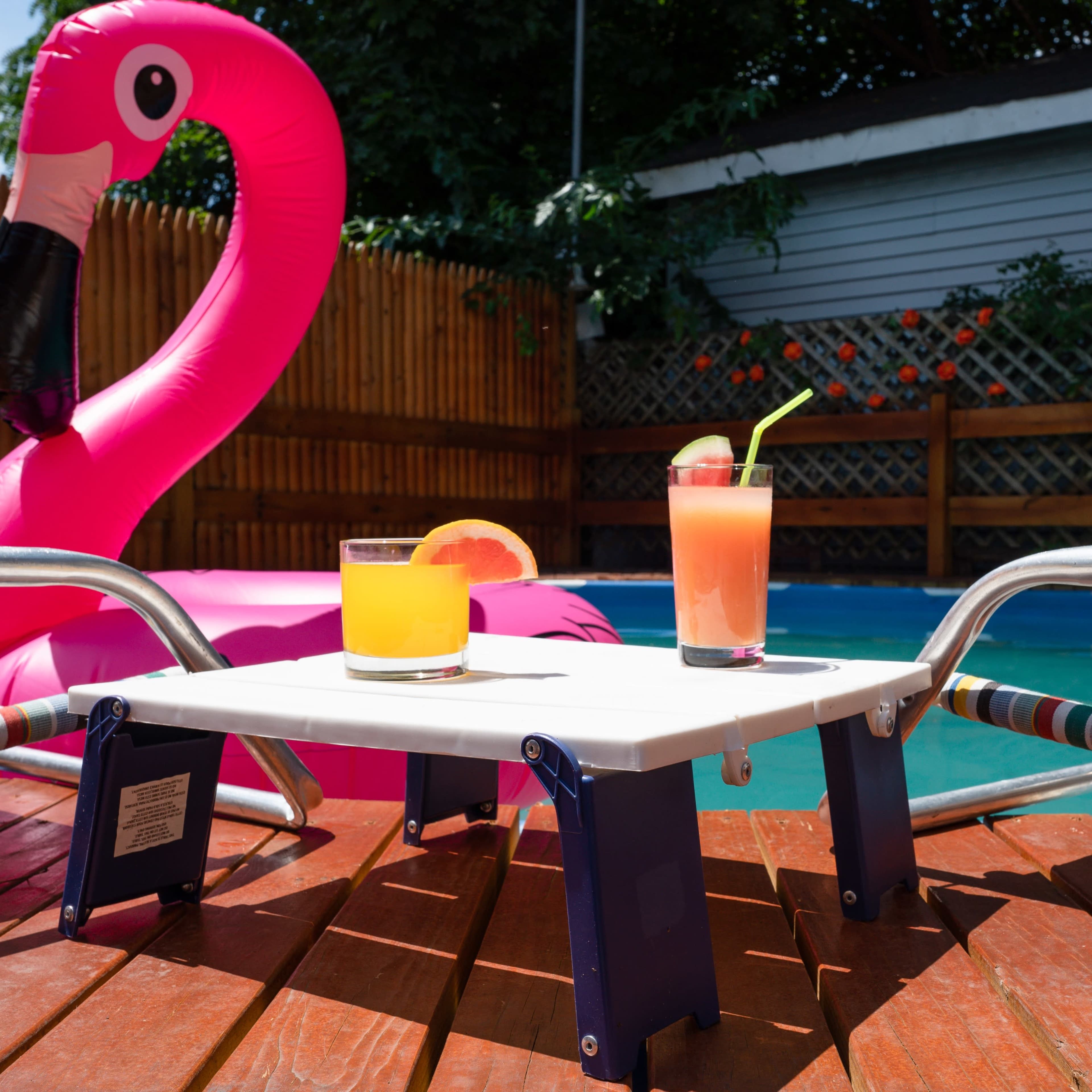 A table holds two colorful cocktails beside a pink inflatable flamingo by a swimming pool.