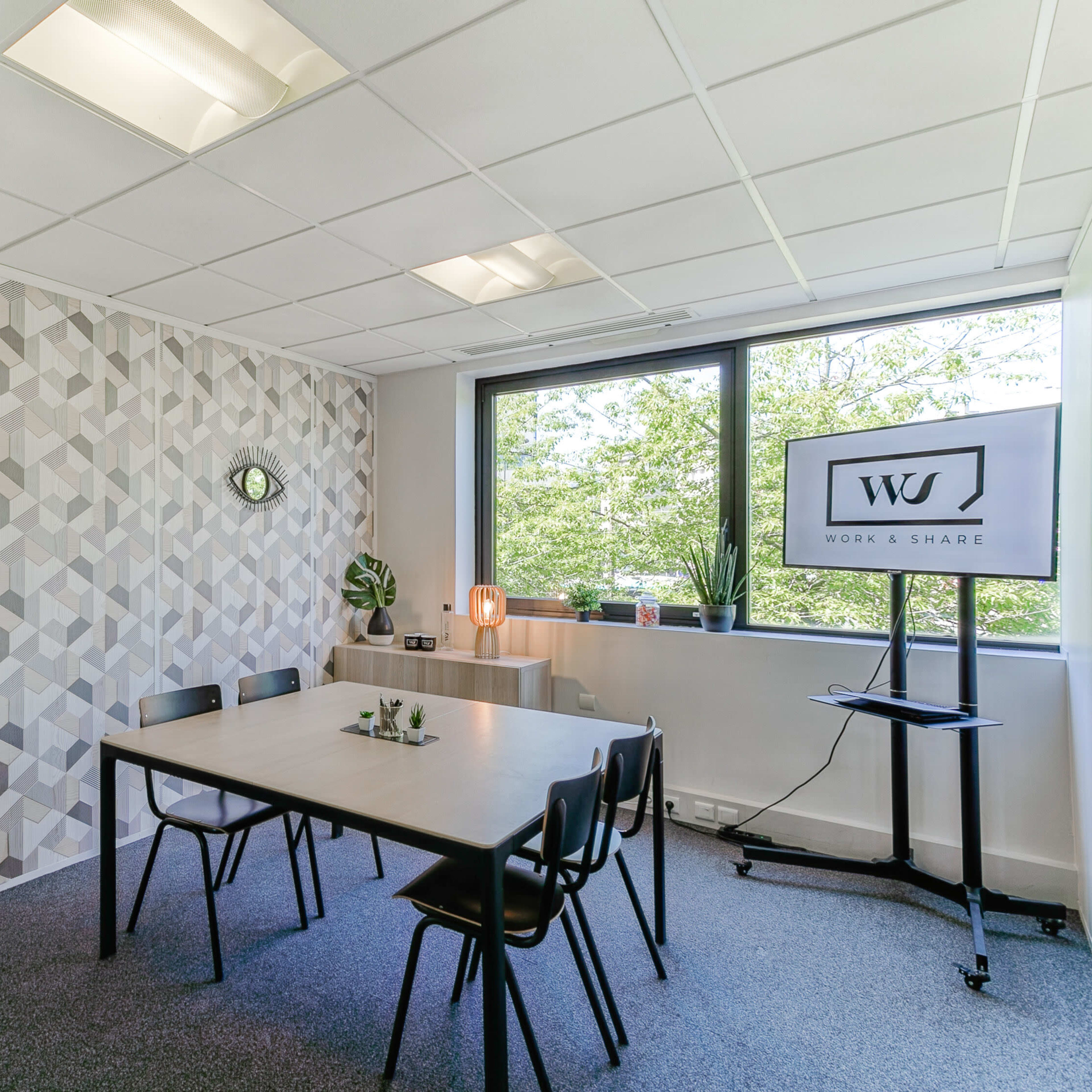 A modern meeting room with a geometric-patterned wall, a table with chairs, a whiteboard, and a screen displaying a logo.