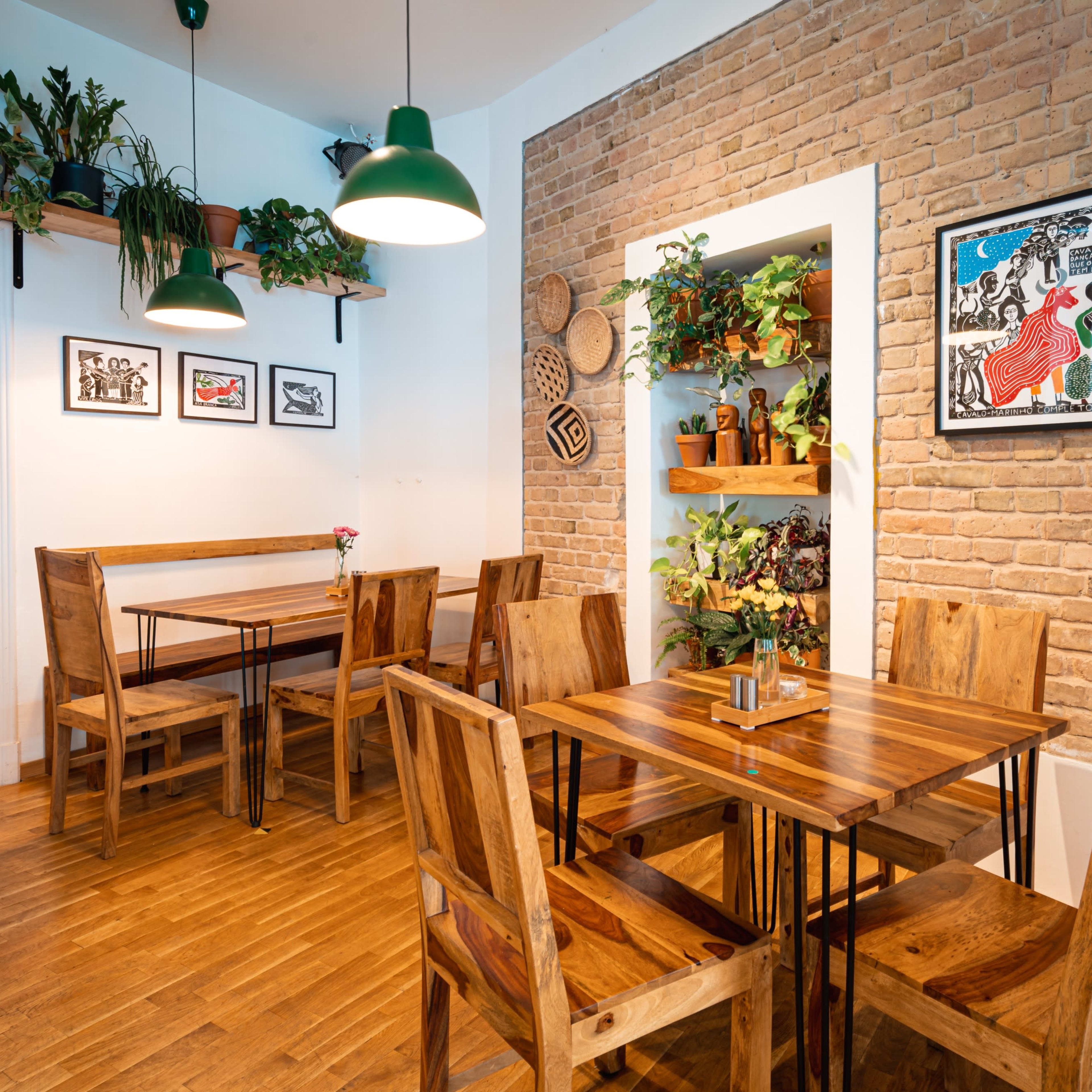 A cozy café interior featuring wooden tables and chairs, brick walls adorned with plants and artwork.