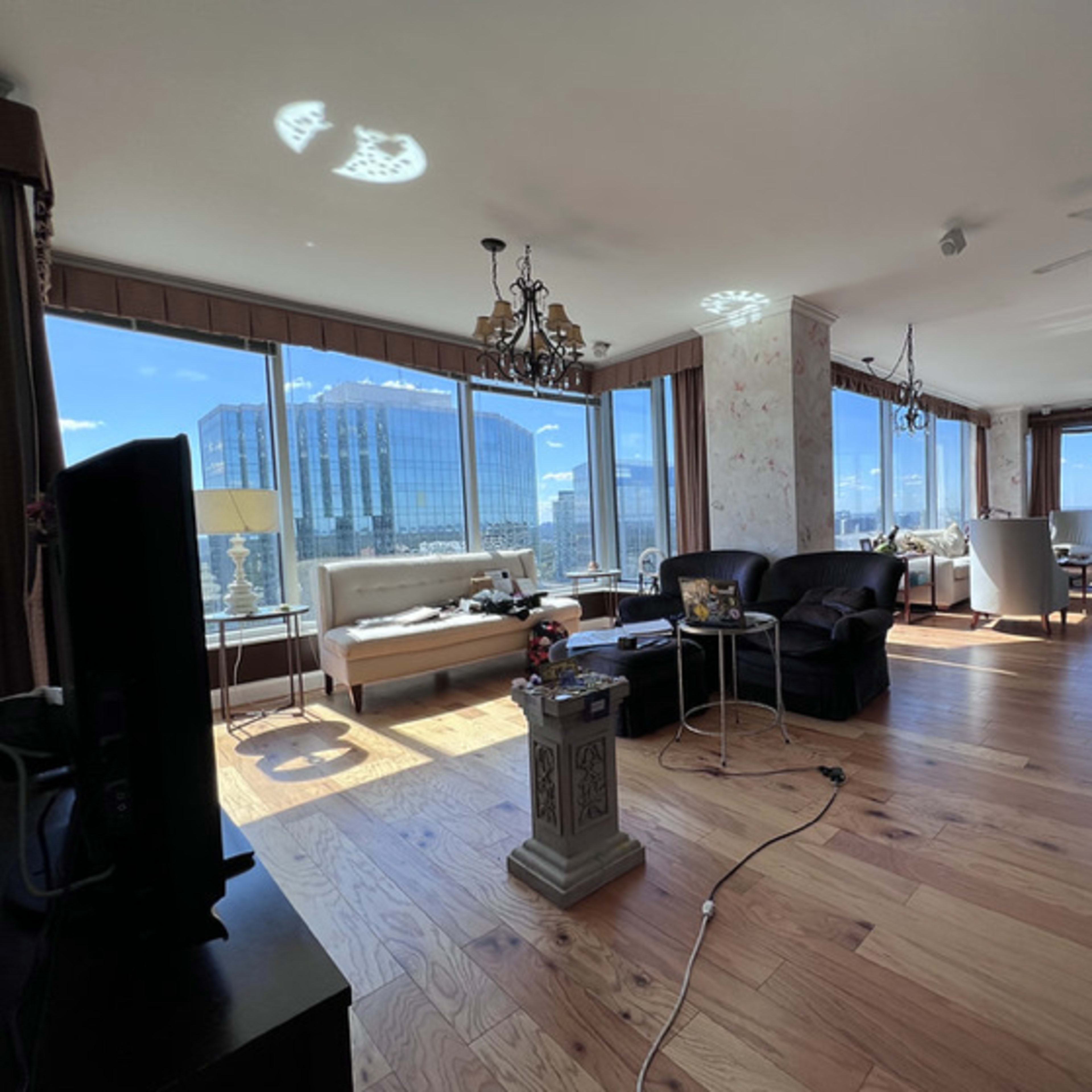 A spacious, modern living room with large windows, wooden flooring, and various pieces of furniture.