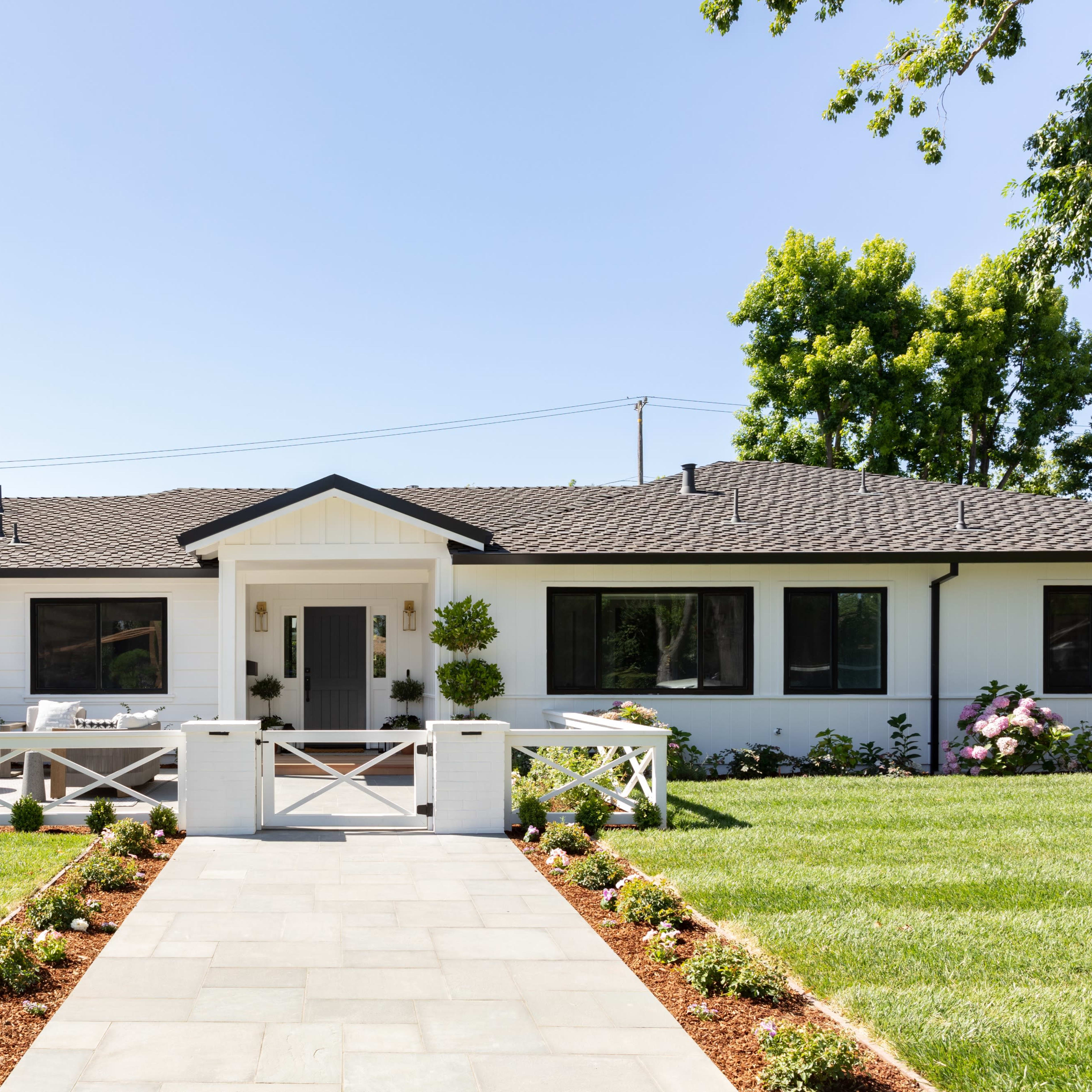 A modern, single-story house with a white facade and a landscaped front yard featuring a stone walkway.