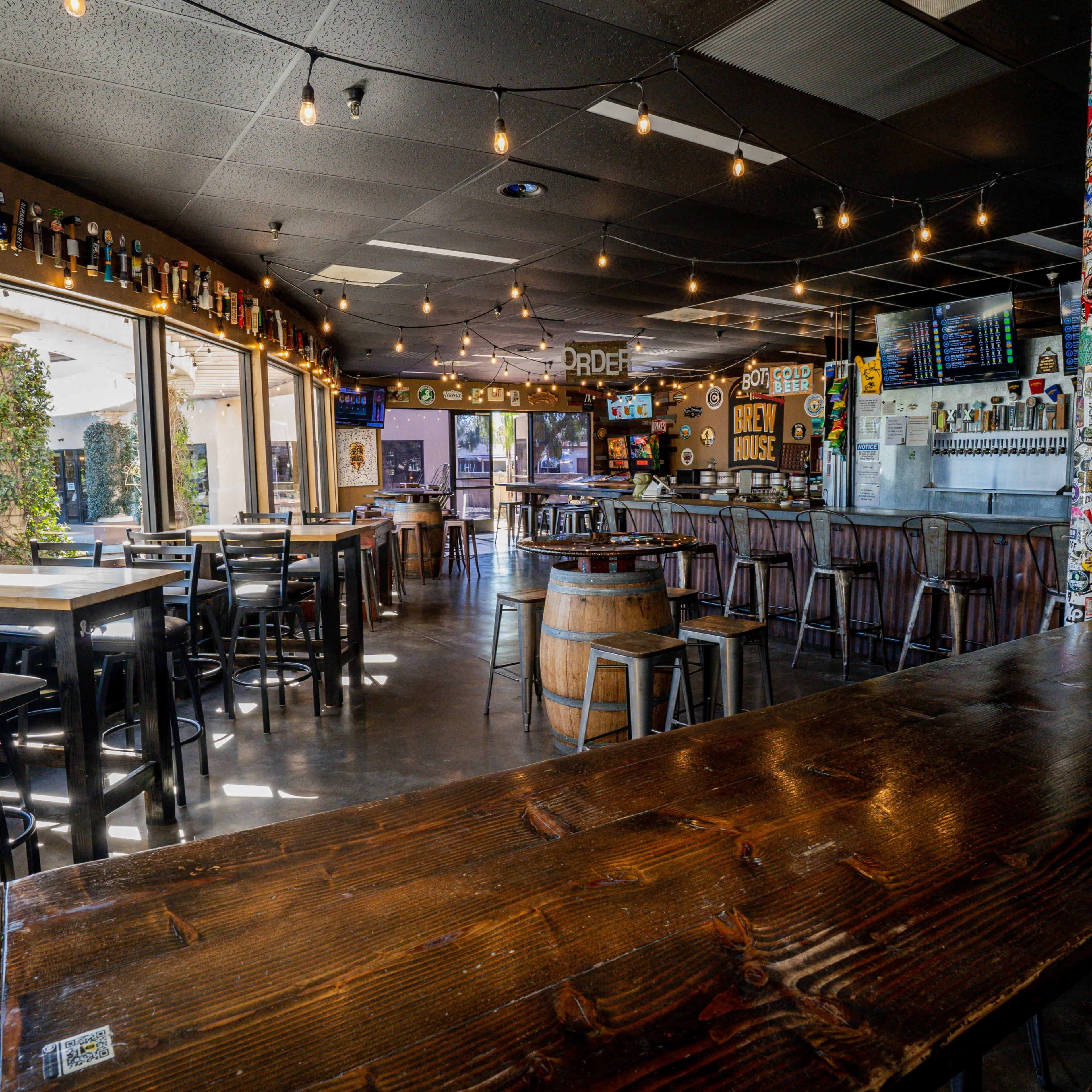 A casual bar with ample seating, large windows, and various beer taps displayed behind the counter.
