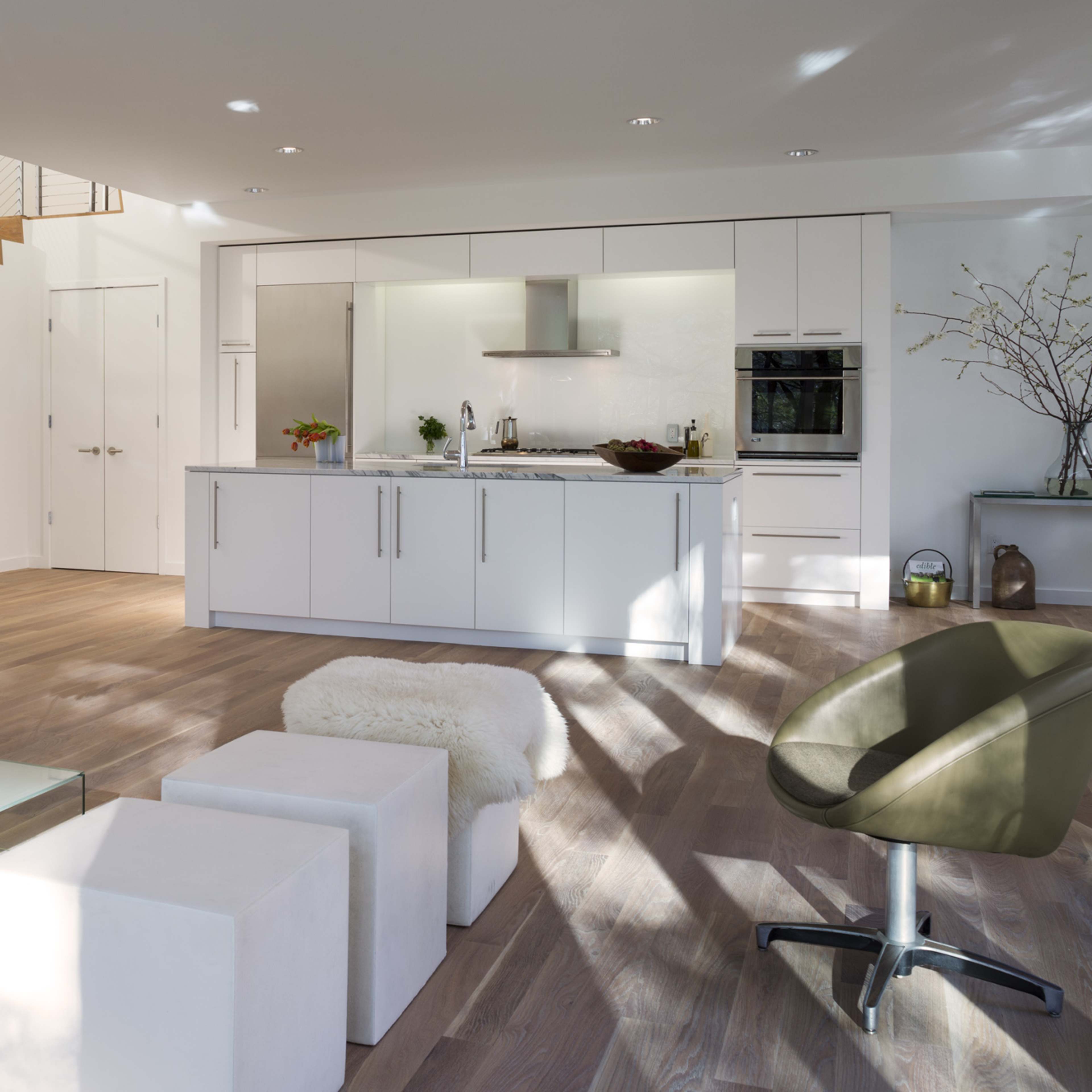 A modern, open-concept living space featuring a kitchen with white cabinetry, a sitting area with a gray sofa, and a staircase in the background.