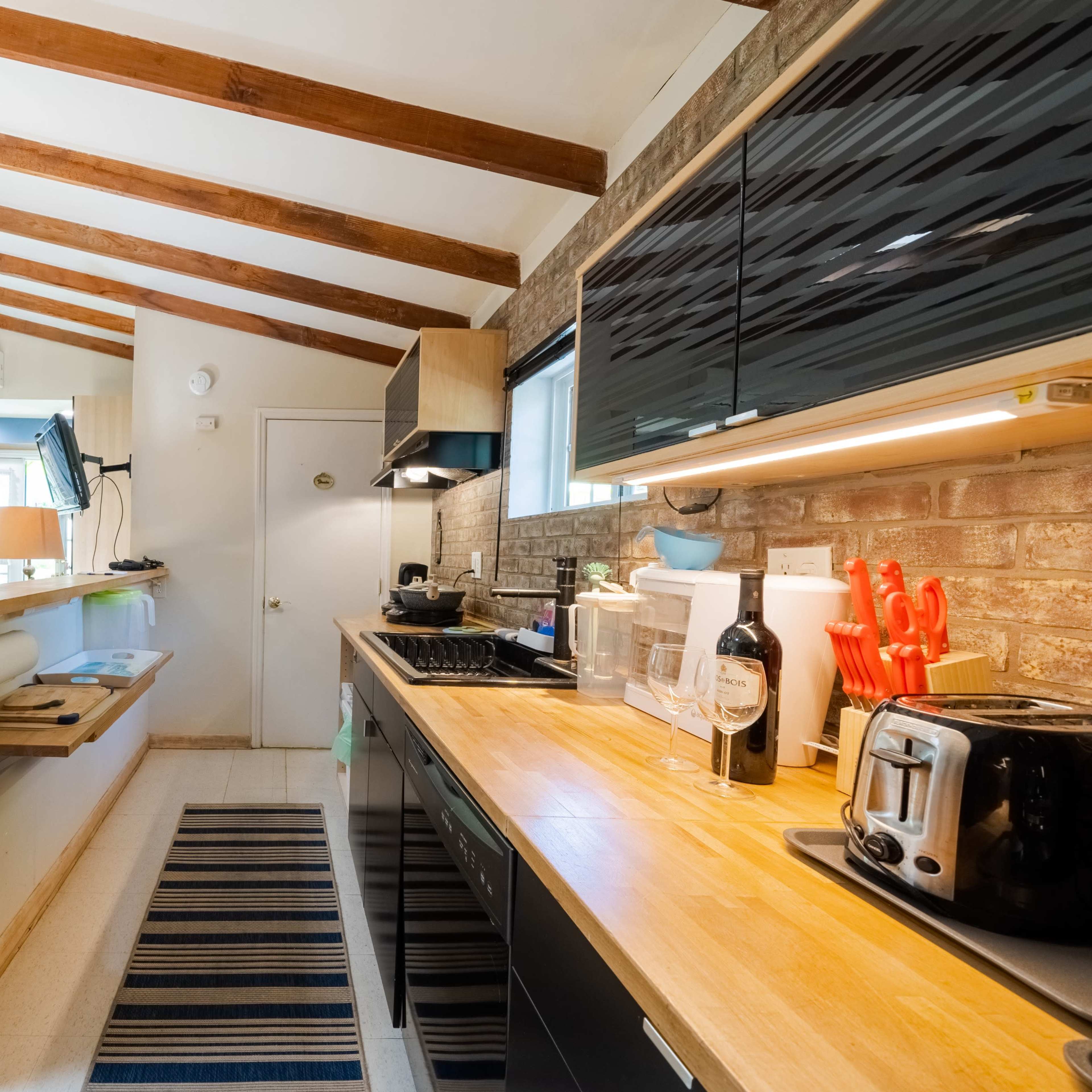 The kitchen features wooden beams on the ceiling, a black countertop, and a dining area with a wooden table and chairs.