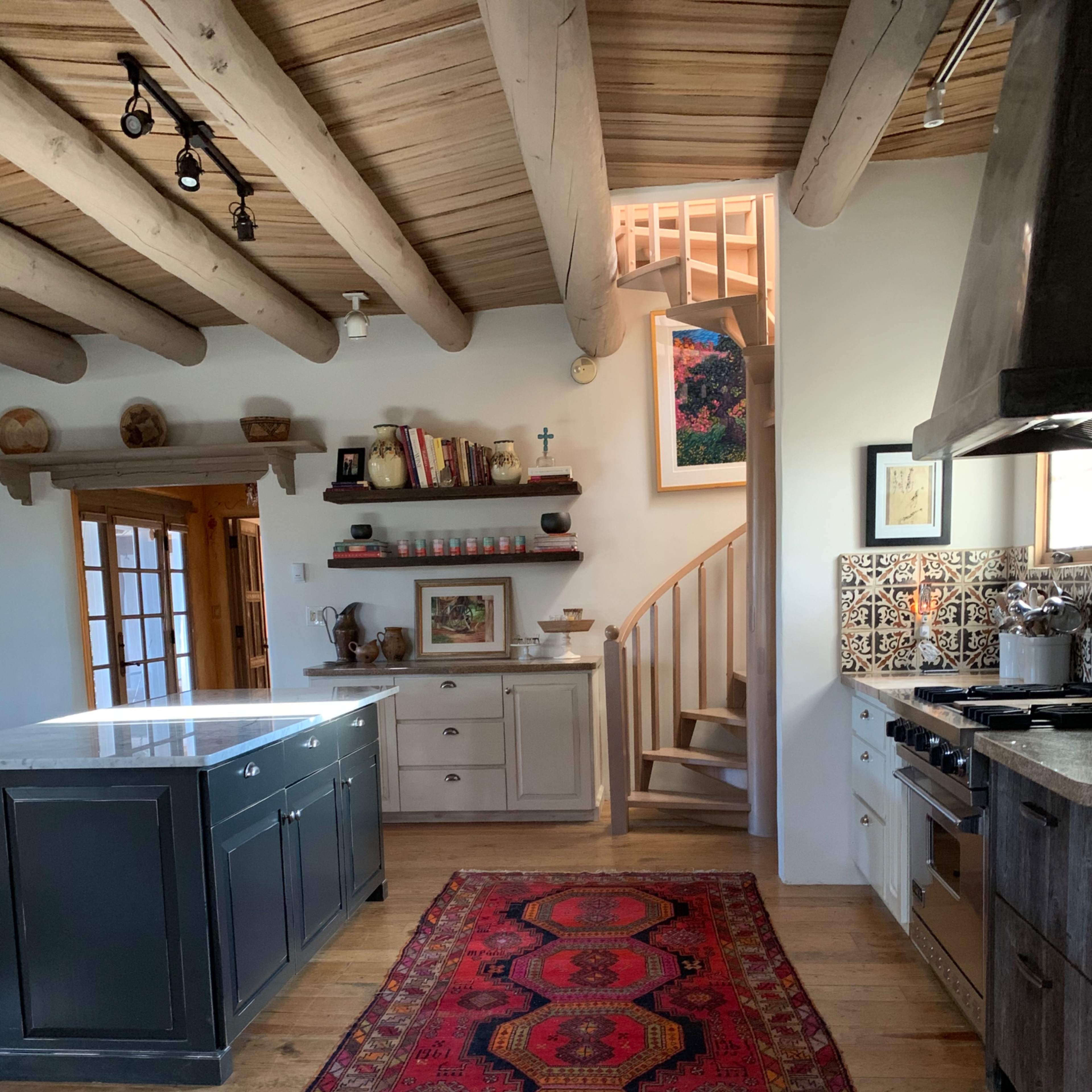 A kitchen with a central island, a red patterned rug on the wooden floor, and a spiral staircase leading to an upper level.