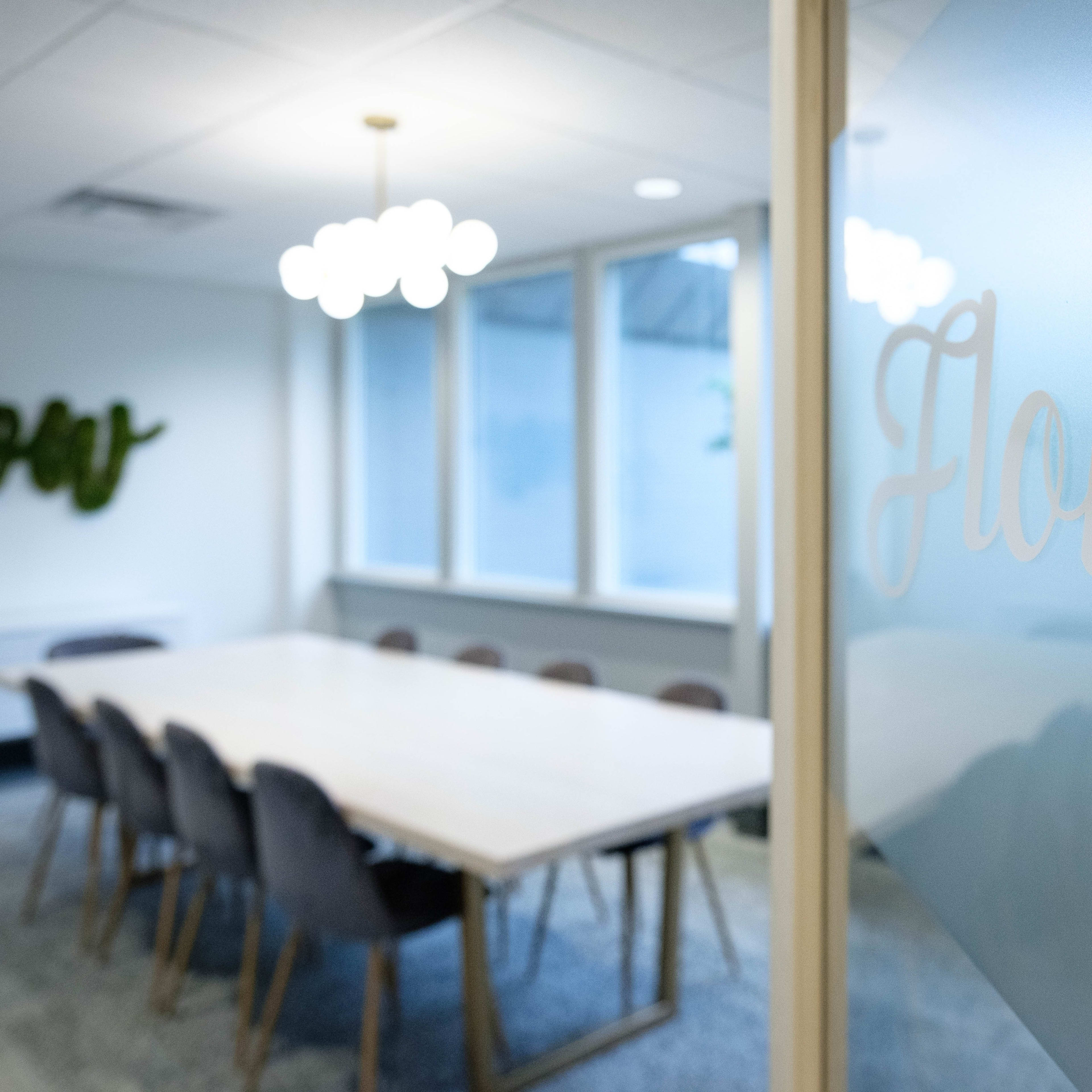 A conference room with a long table surrounded by chairs, illuminated by pendant lights and featuring large windows.