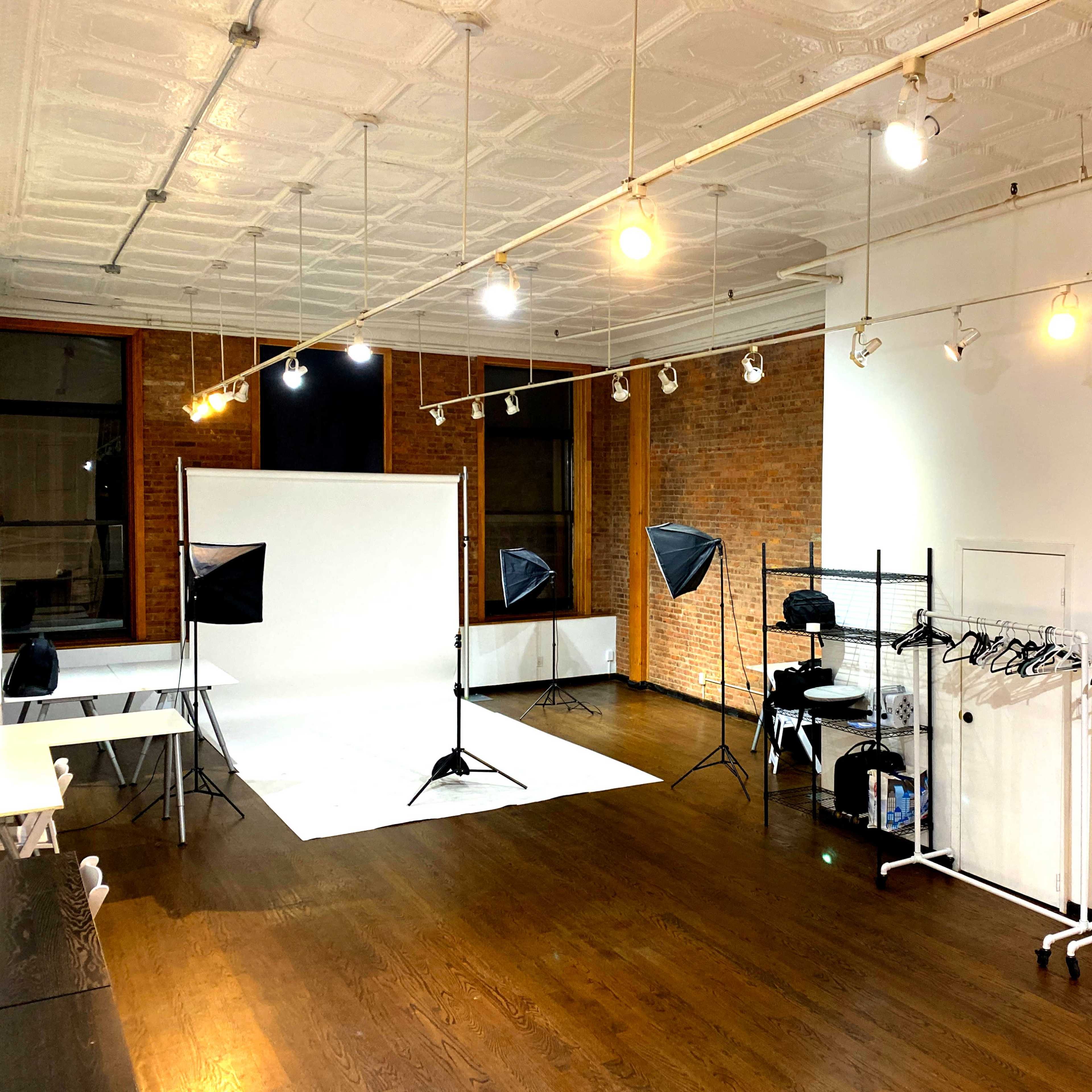 A photography studio with a white backdrop and multiple lighting setups, along with clothing racks along the wall.