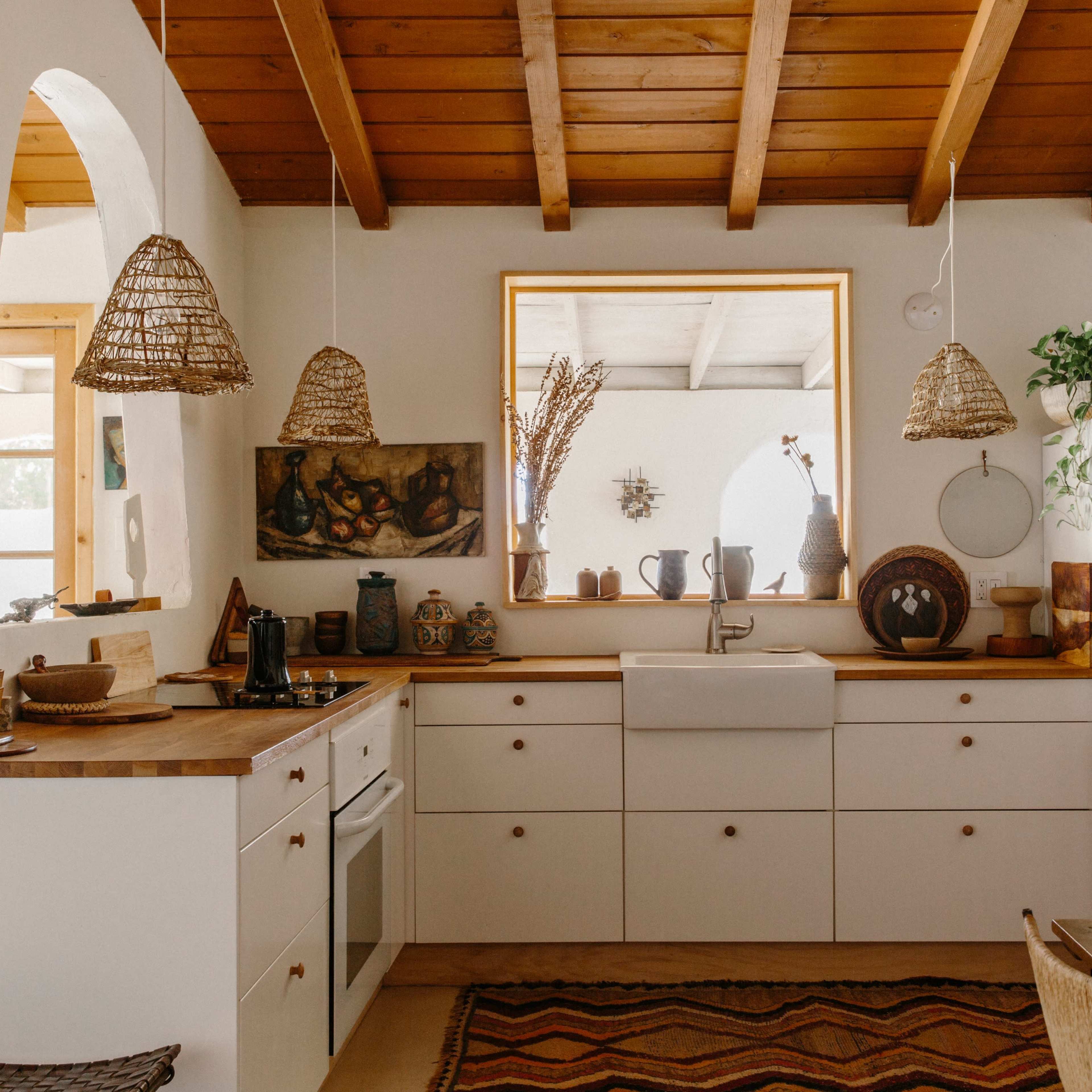 A cozy kitchen with wooden beams, white cabinetry, a farmhouse sink, and woven pendant lights.