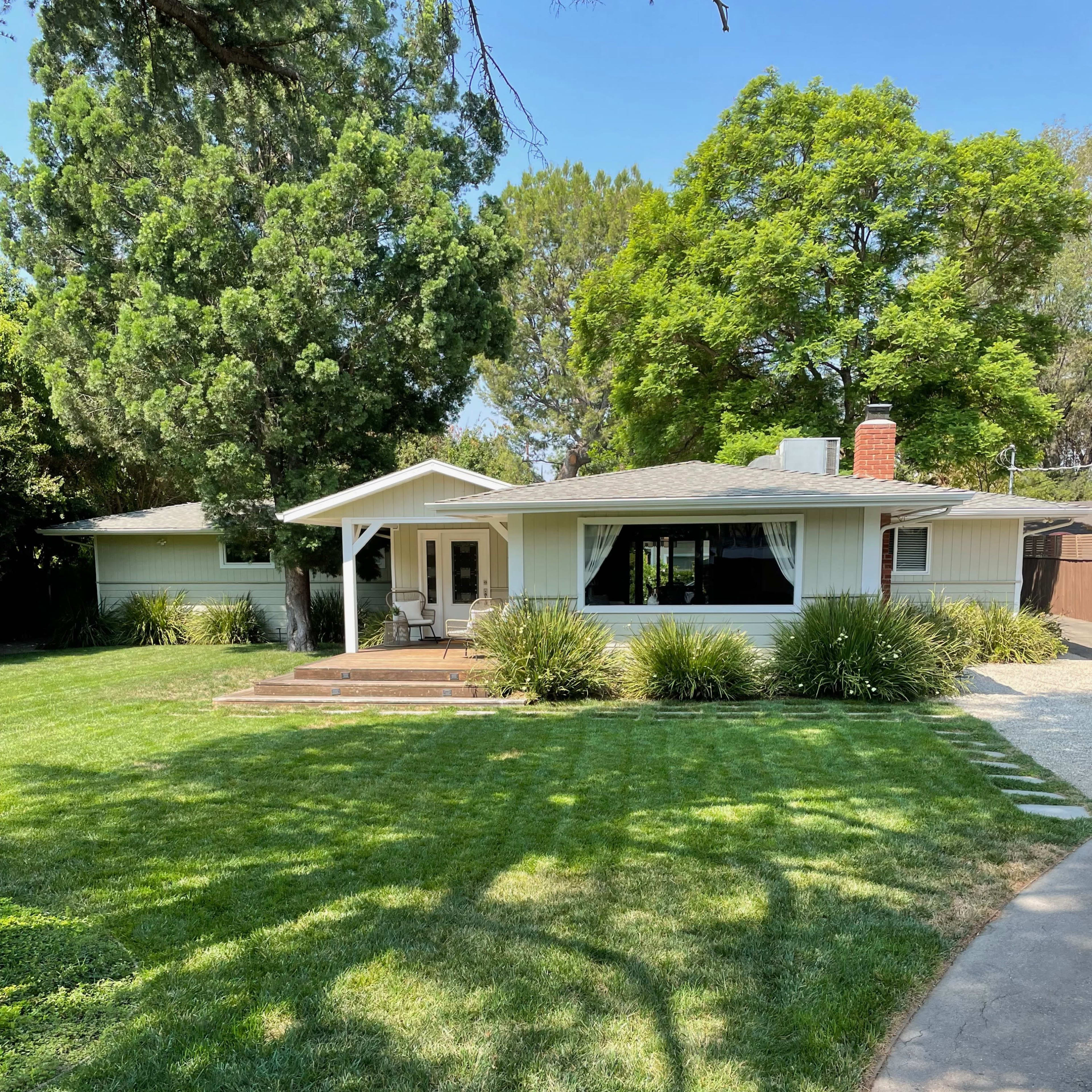 A single-story house with a front porch is nestled among green lawns and trees.