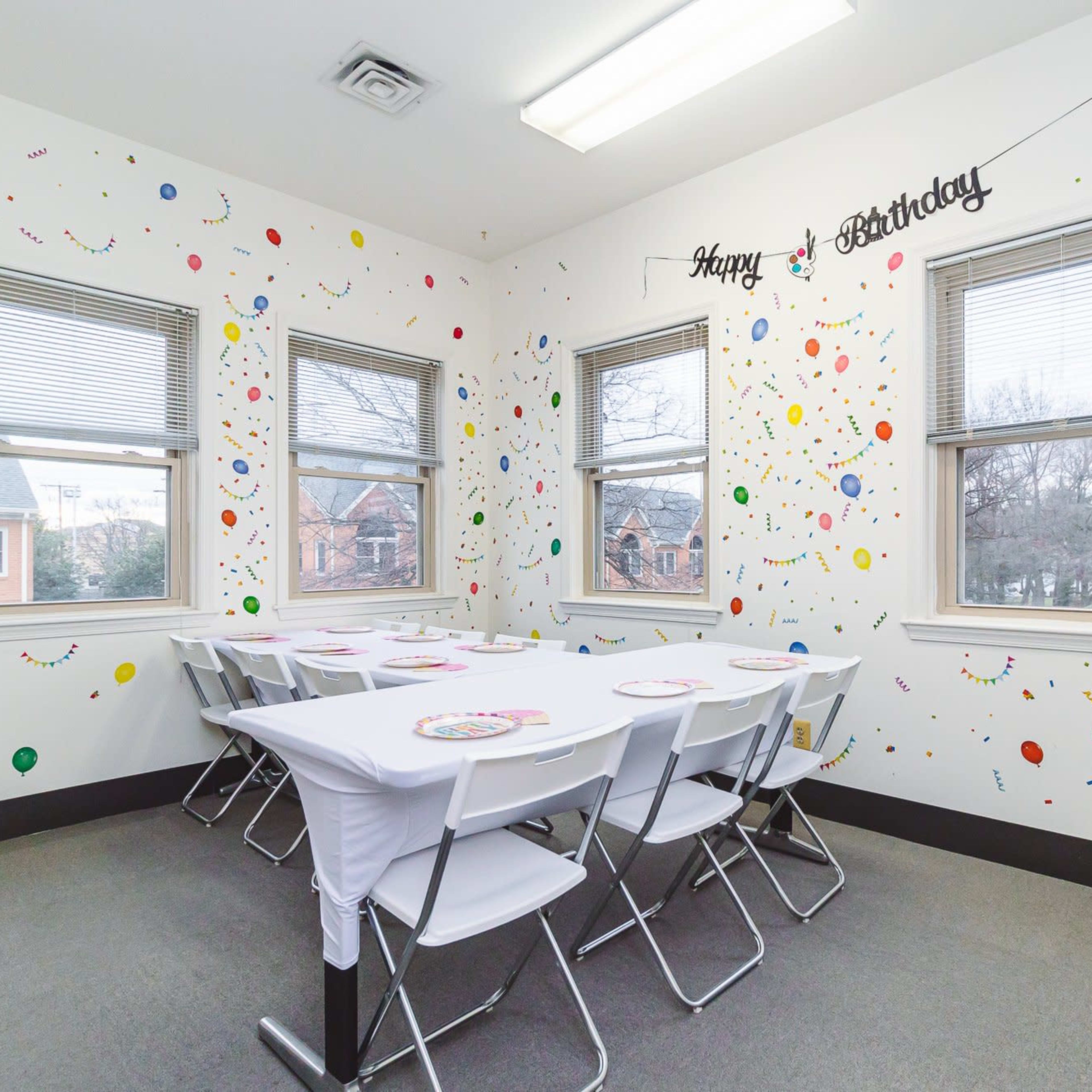 A birthday celebration room with a table set for guests, surrounded by colorful decorations on the walls.