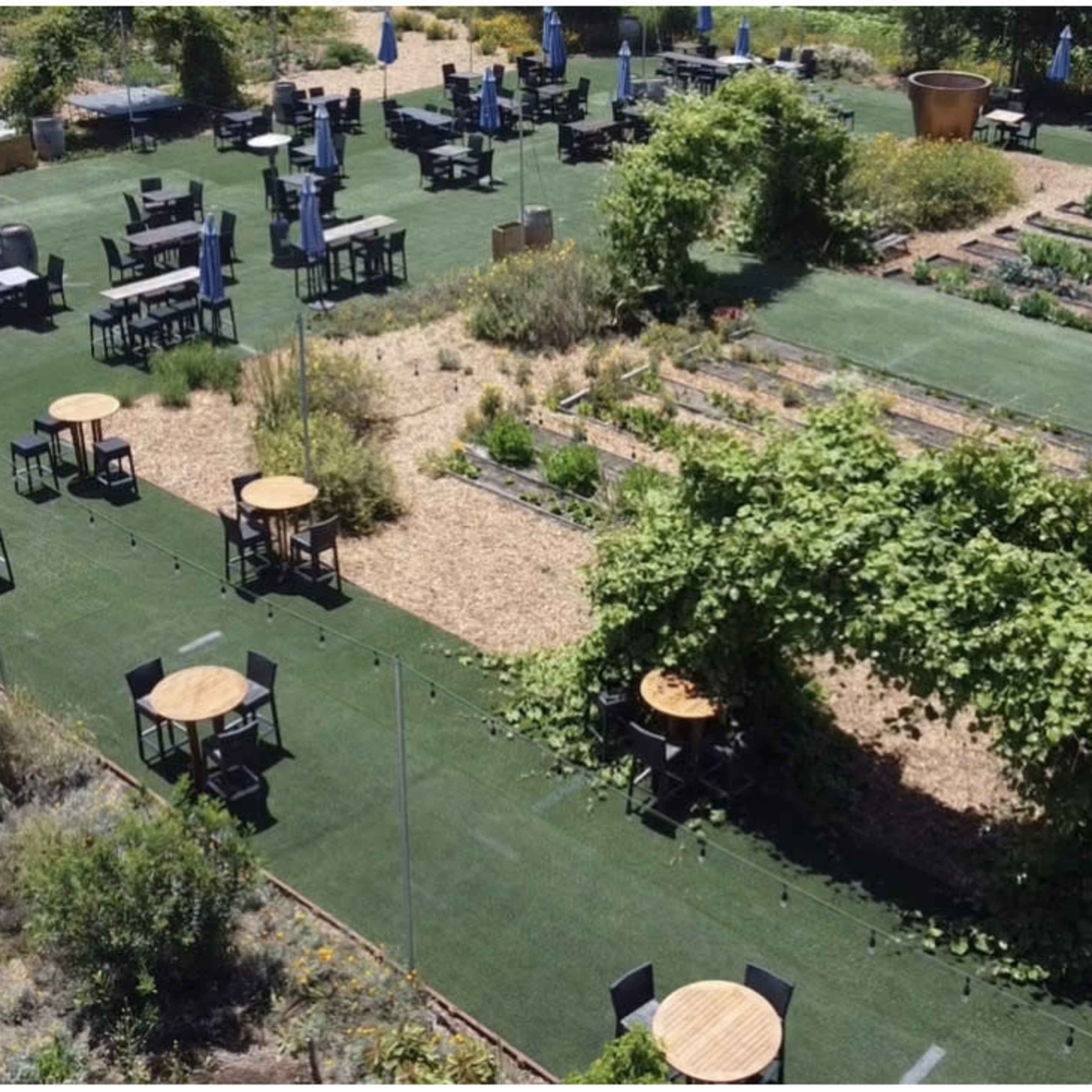 A landscaped outdoor dining area with tables and chairs set among garden beds and greenery.