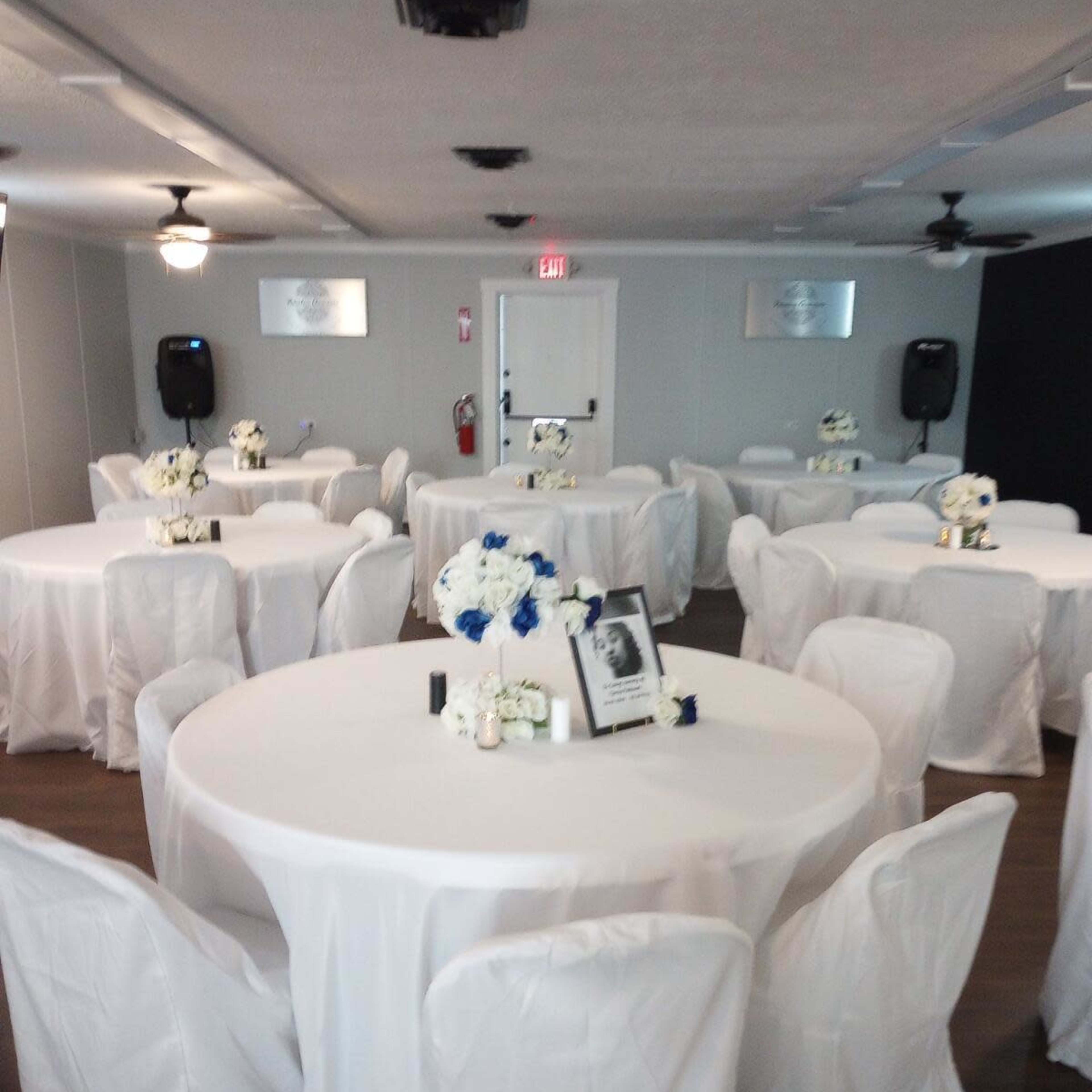 A banquet hall with round tables covered in white cloth and adorned with floral centerpieces.