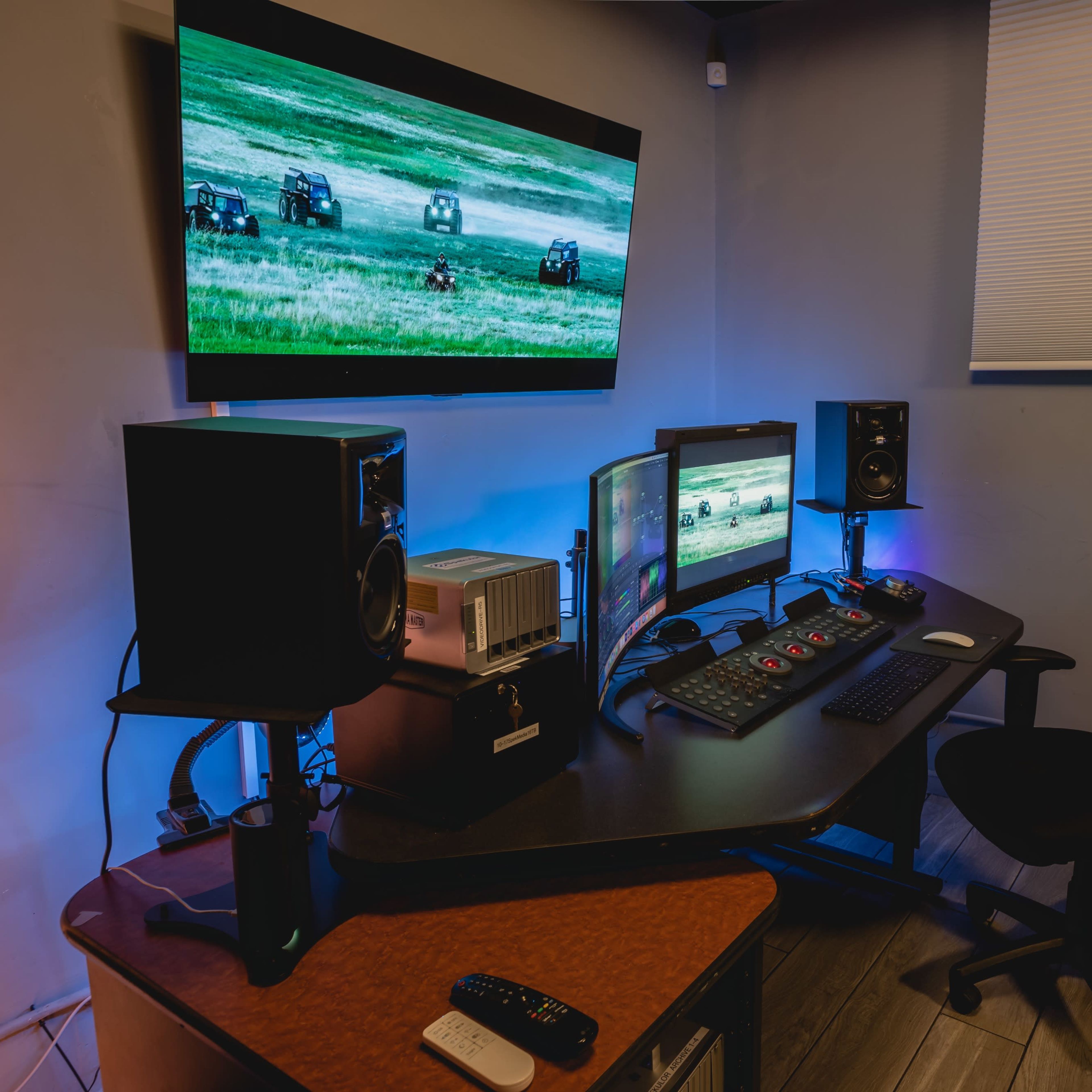 A recording studio setup featuring multiple monitors, speakers, and a control panel in a well-lit room.