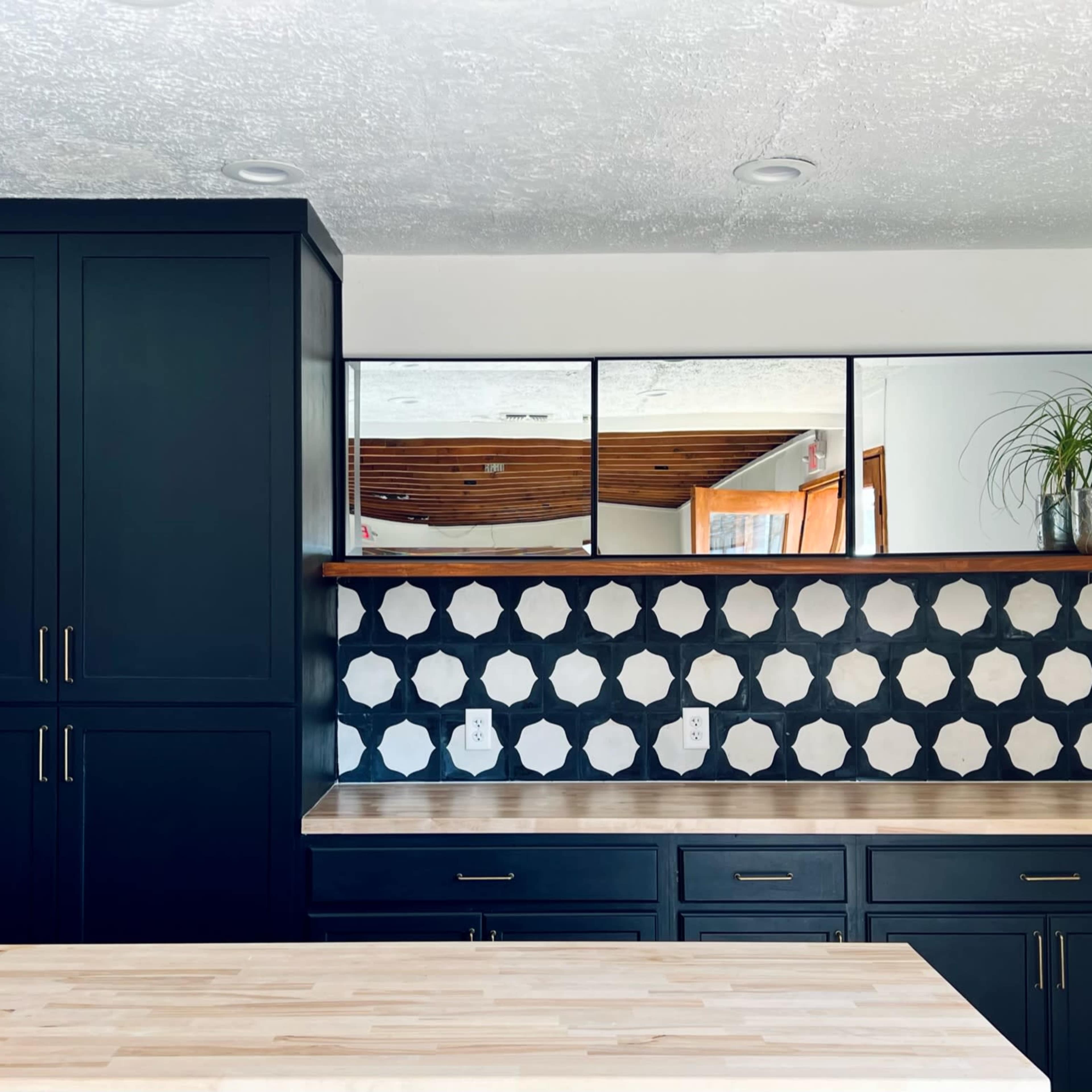 A modern kitchen featuring dark cabinetry, a light wooden countertop, and a backsplash with a geometric, black-and-white tile pattern.