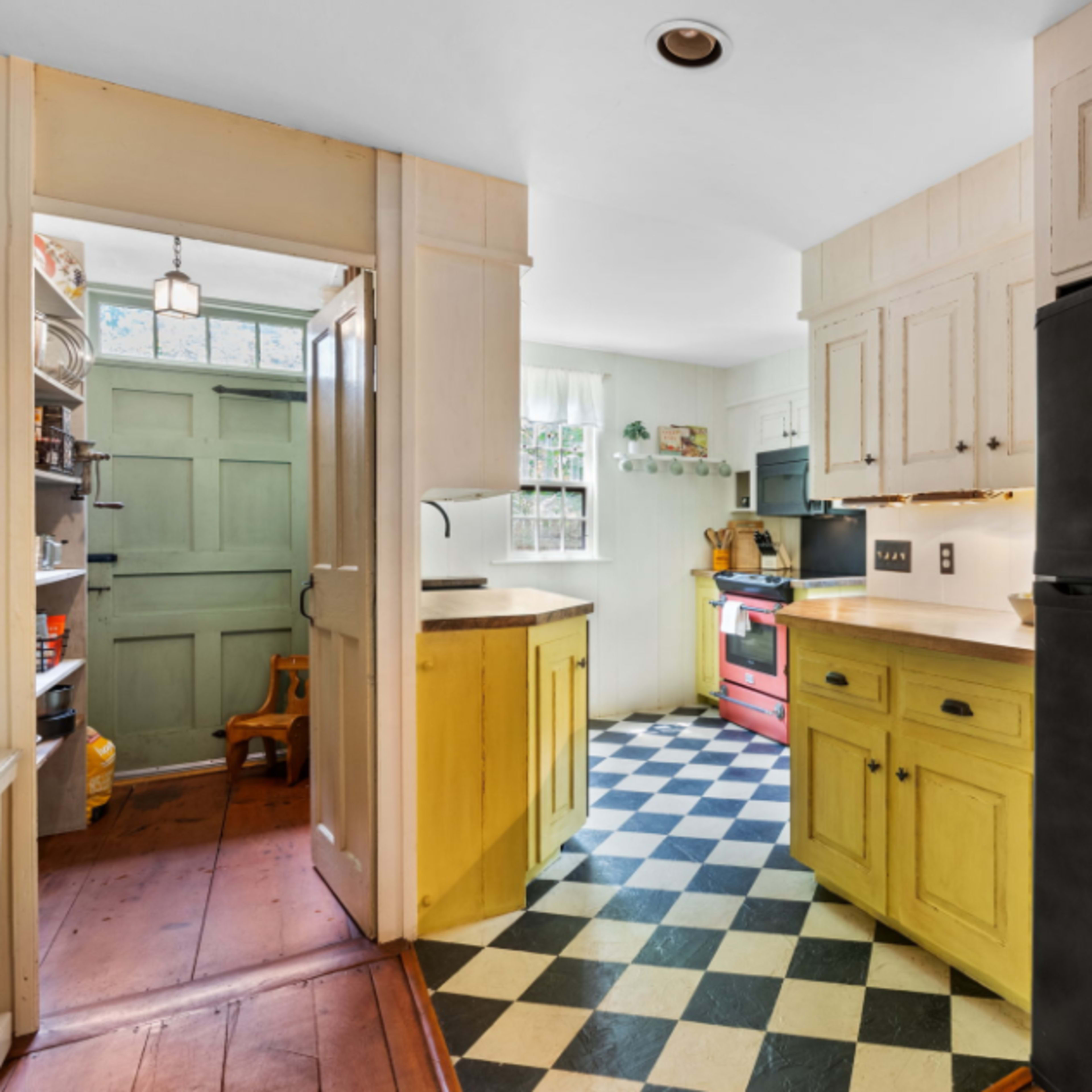 A kitchen with yellow cabinets, a black refrigerator, a checkered floor, and an adjoining pantry.