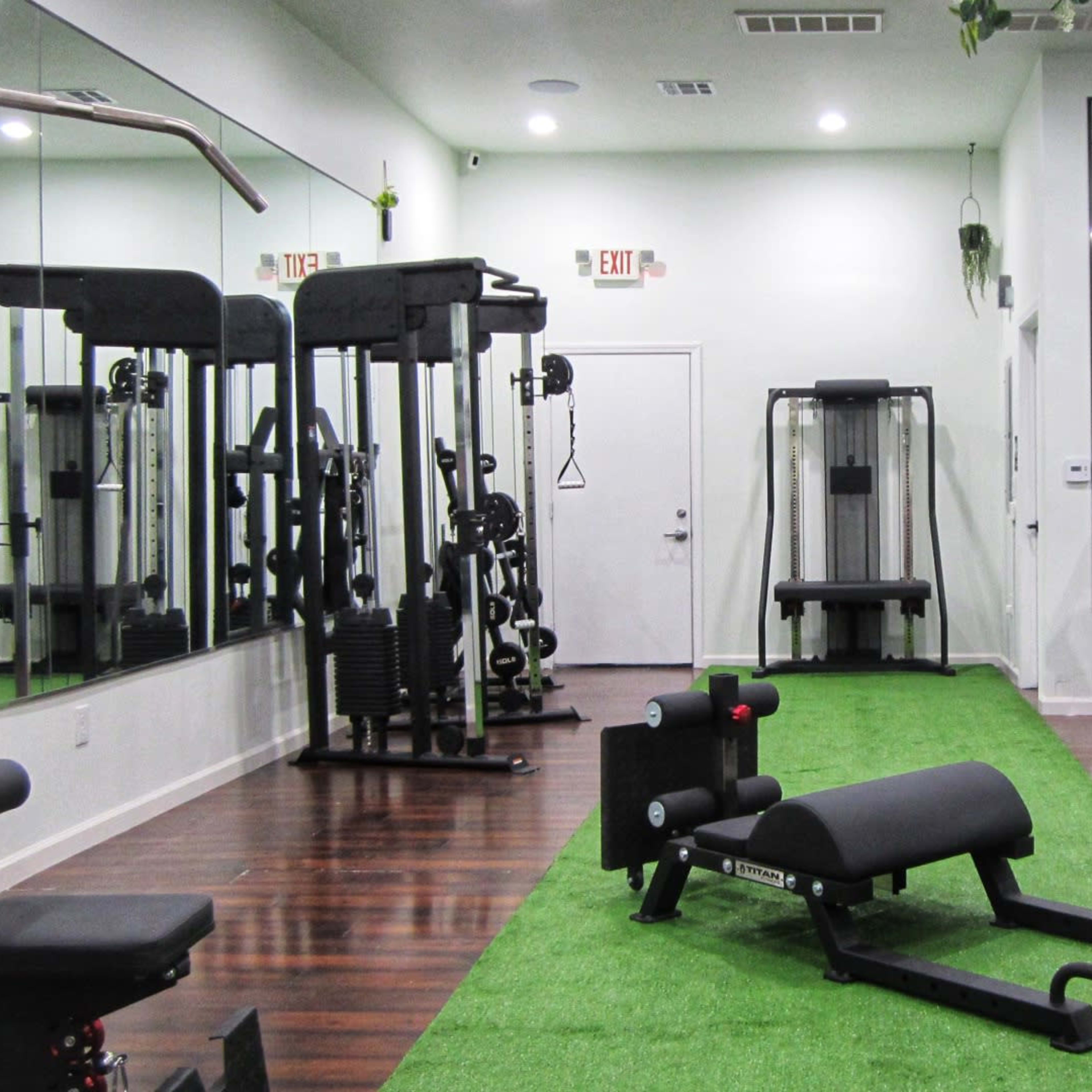 A well-equipped gym with various exercise machines, a weight bench, and green artificial turf flooring.