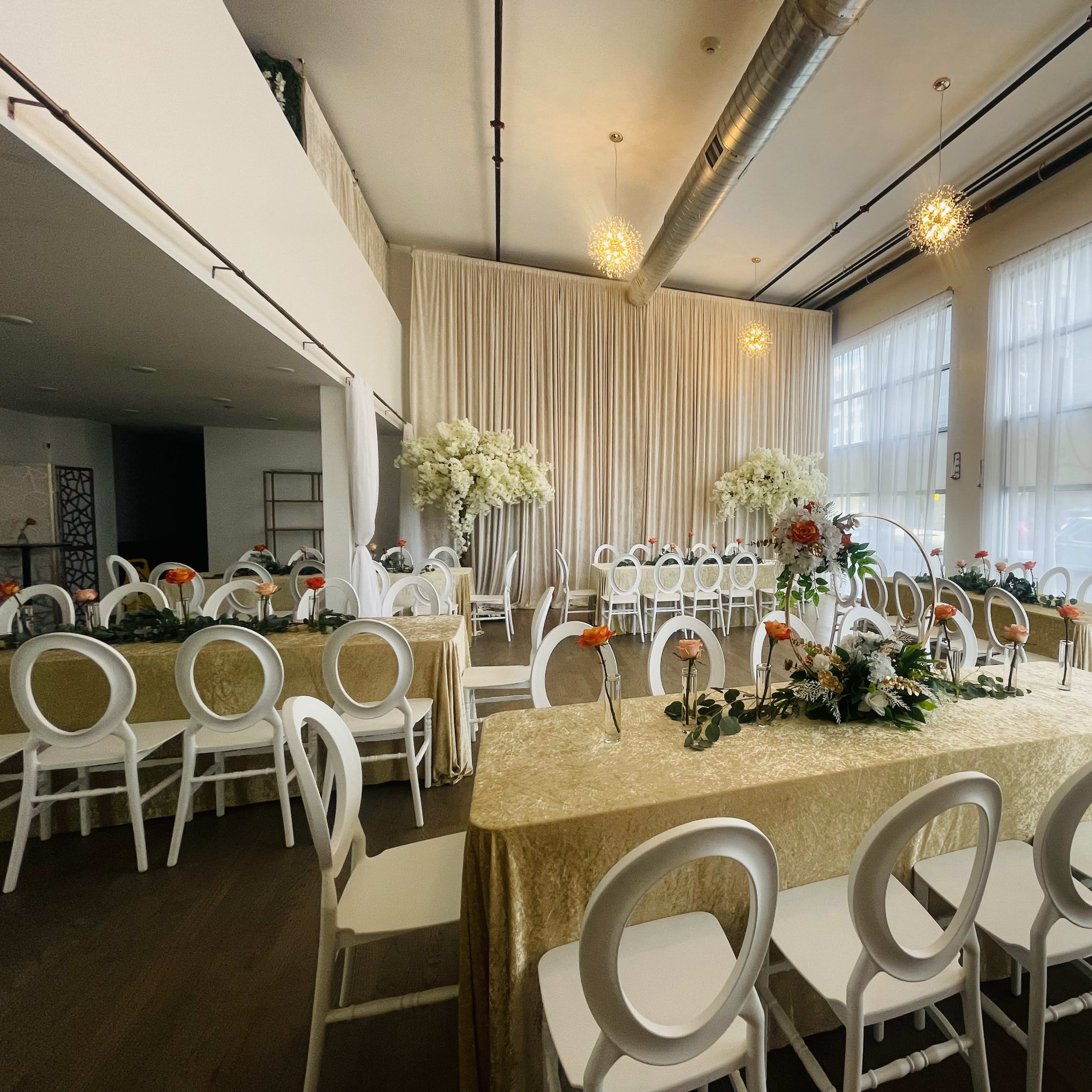 A banquet hall set for an event, featuring elegantly decorated tables with floral arrangements and white chairs arranged in rows.