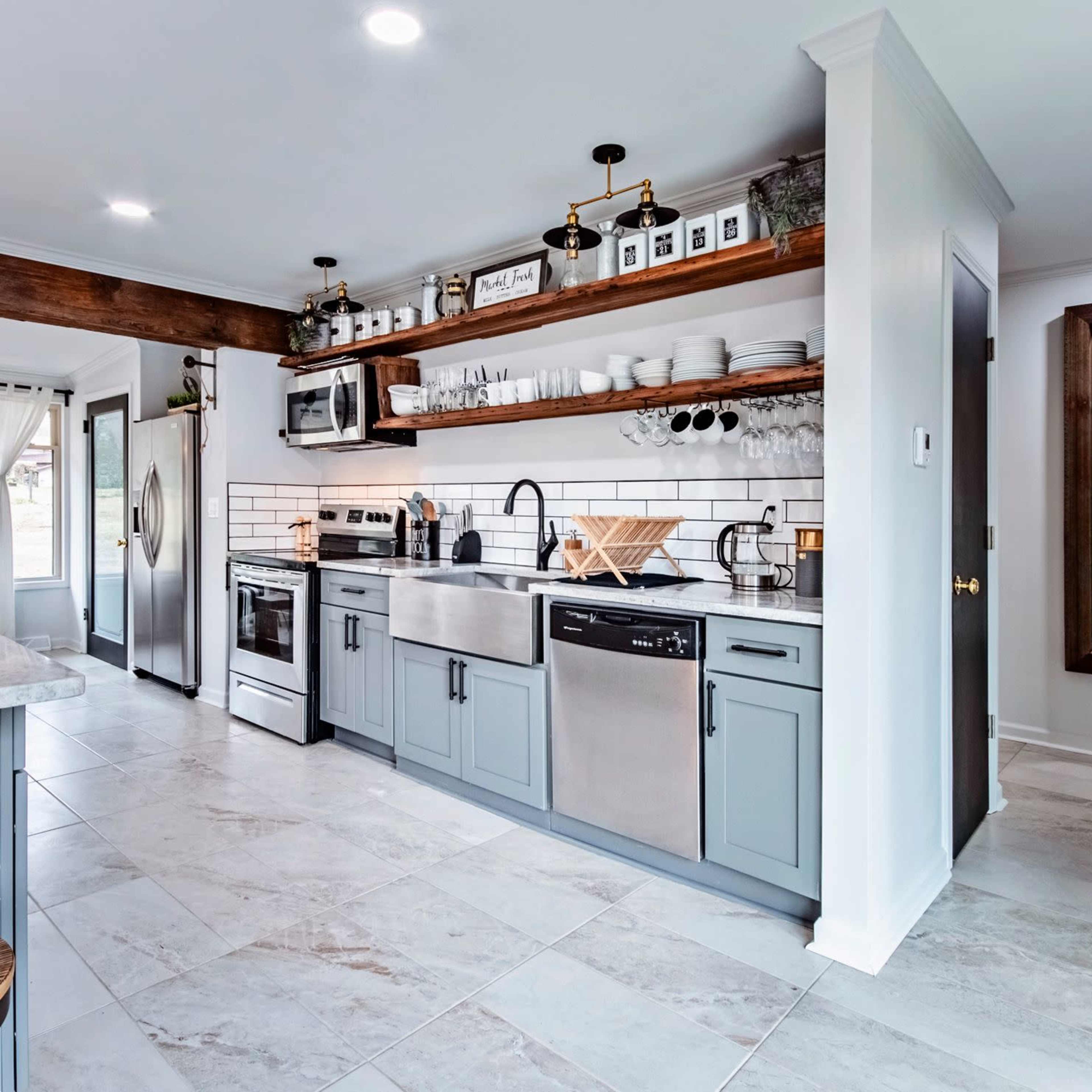 A modern kitchen features gray cabinetry, stainless steel appliances, and open shelving with various kitchen items, illuminated by overhead lights.