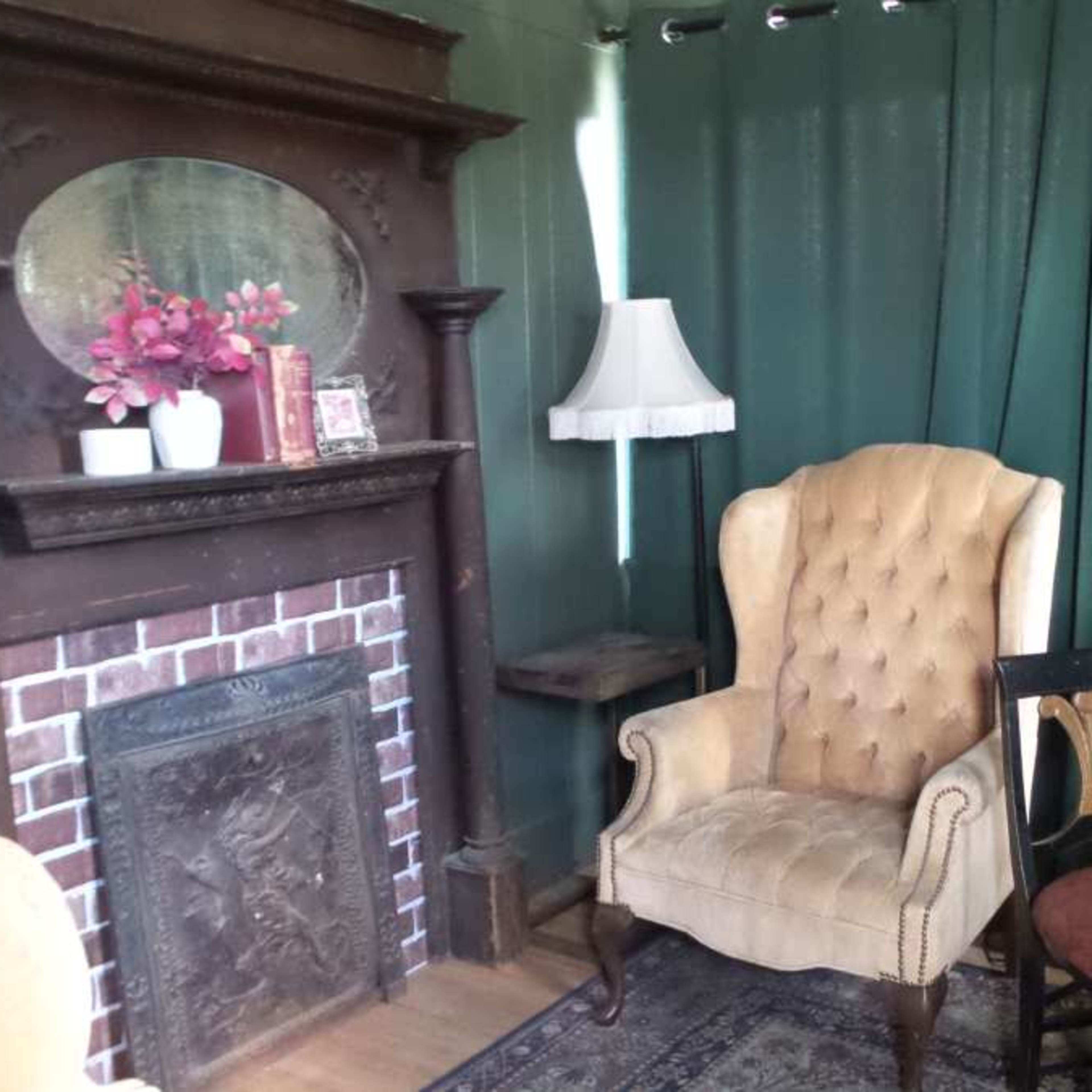 A vintage sitting area with a tufted armchair, a small wooden table, and a fireplace surrounded by a green curtain.