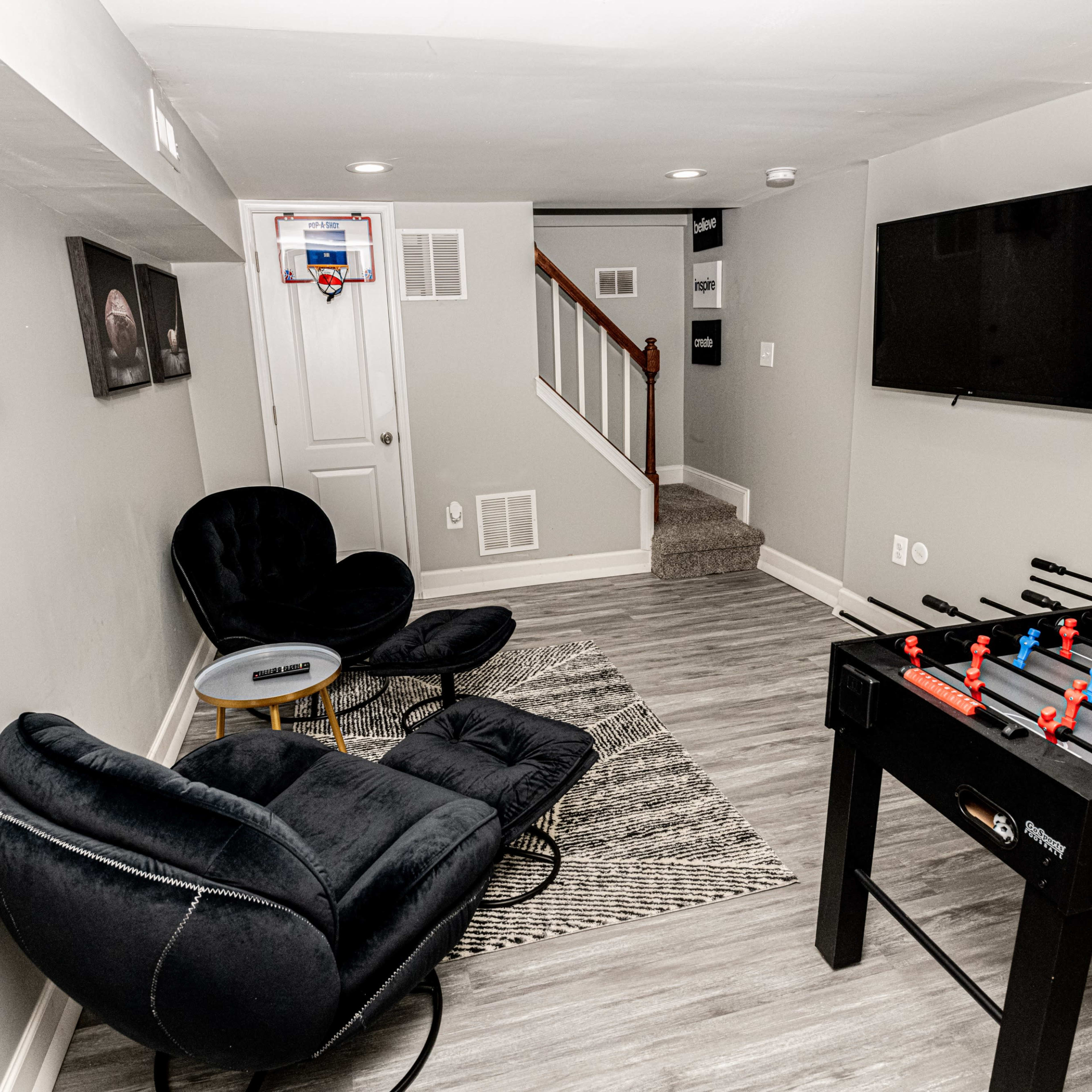 A basement recreation area featuring a foosball table, two black chairs, a patterned rug, and a small wall-mounted basketball hoop.