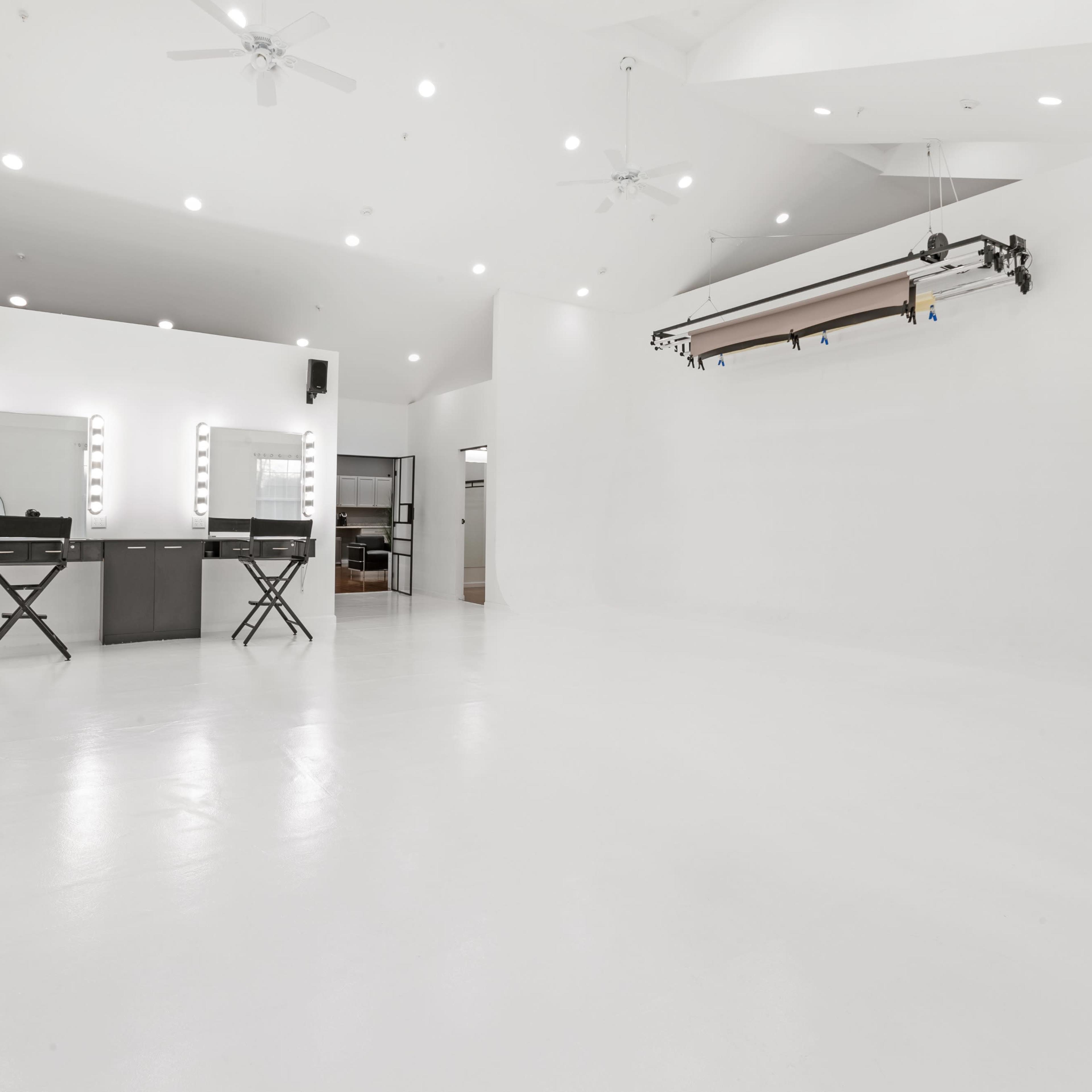 A spacious, well-lit studio features two makeup mirrors and a backdrop support system against a white wall.