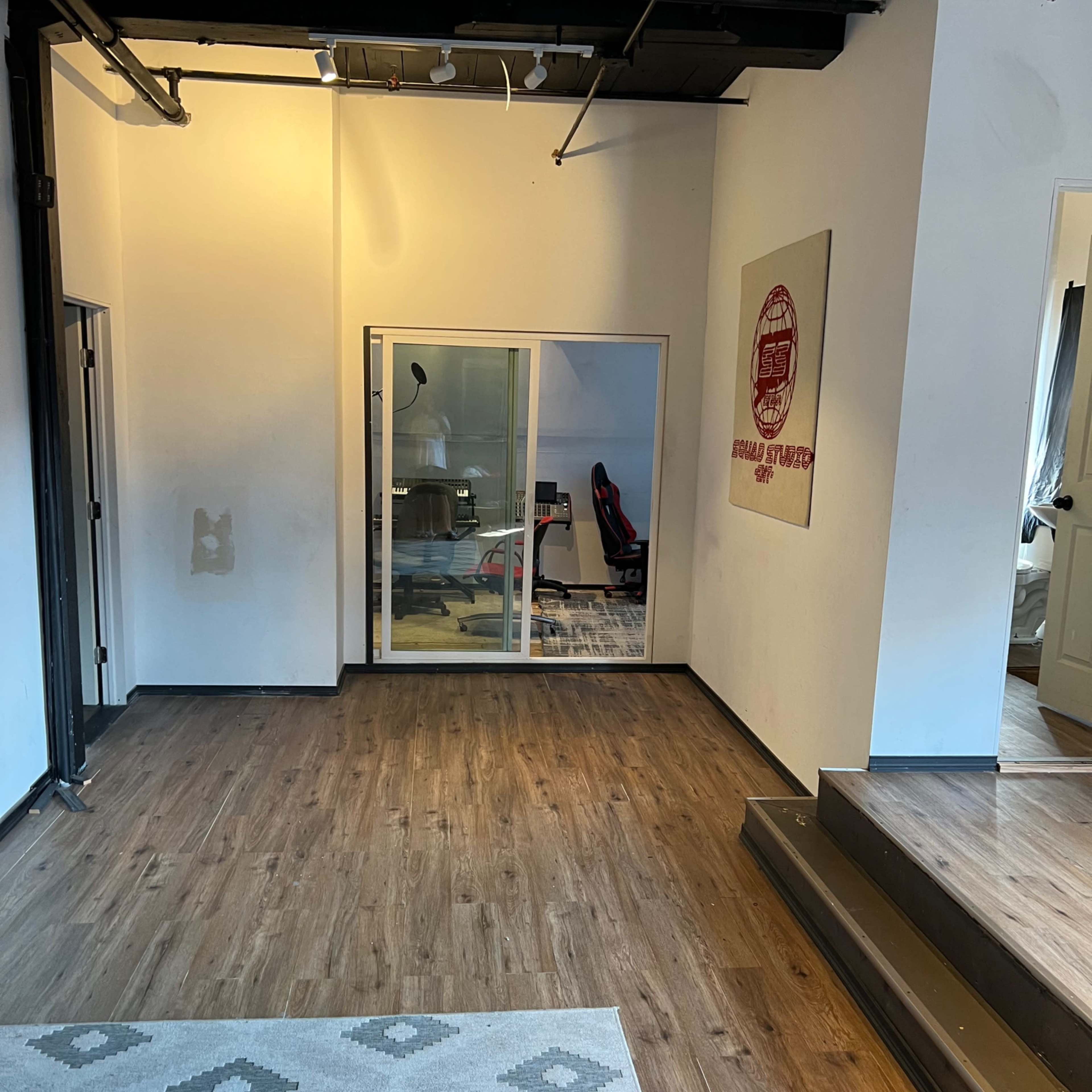 A spacious office area with wooden flooring, a large area rug, and a glass-walled meeting room visible in the background.