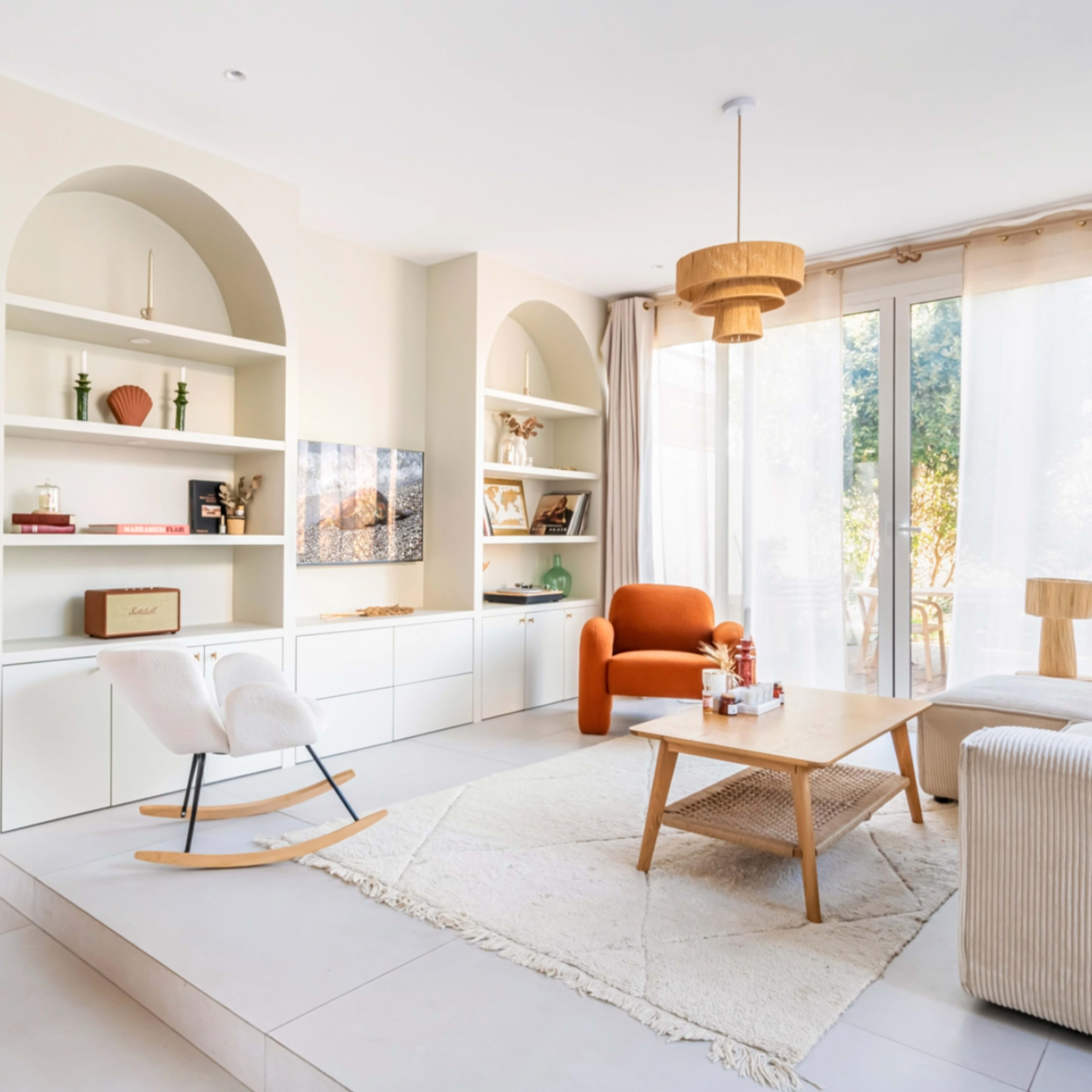 A modern living room with built-in shelves, a rocking chair, and large windows allowing natural light to enter the space.