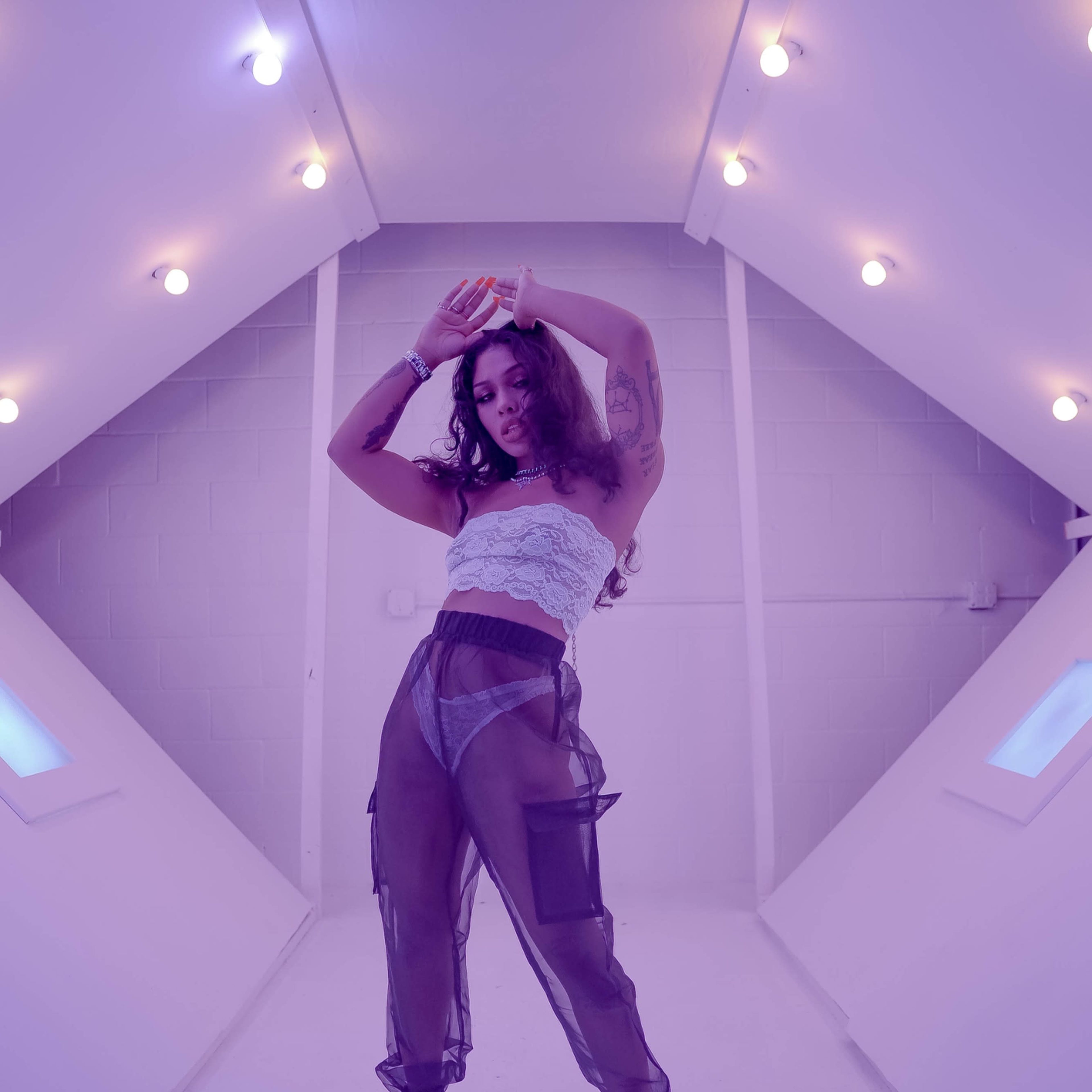 A person poses with their arms raised in a well-lit, angular room featuring white walls and glowing lights.