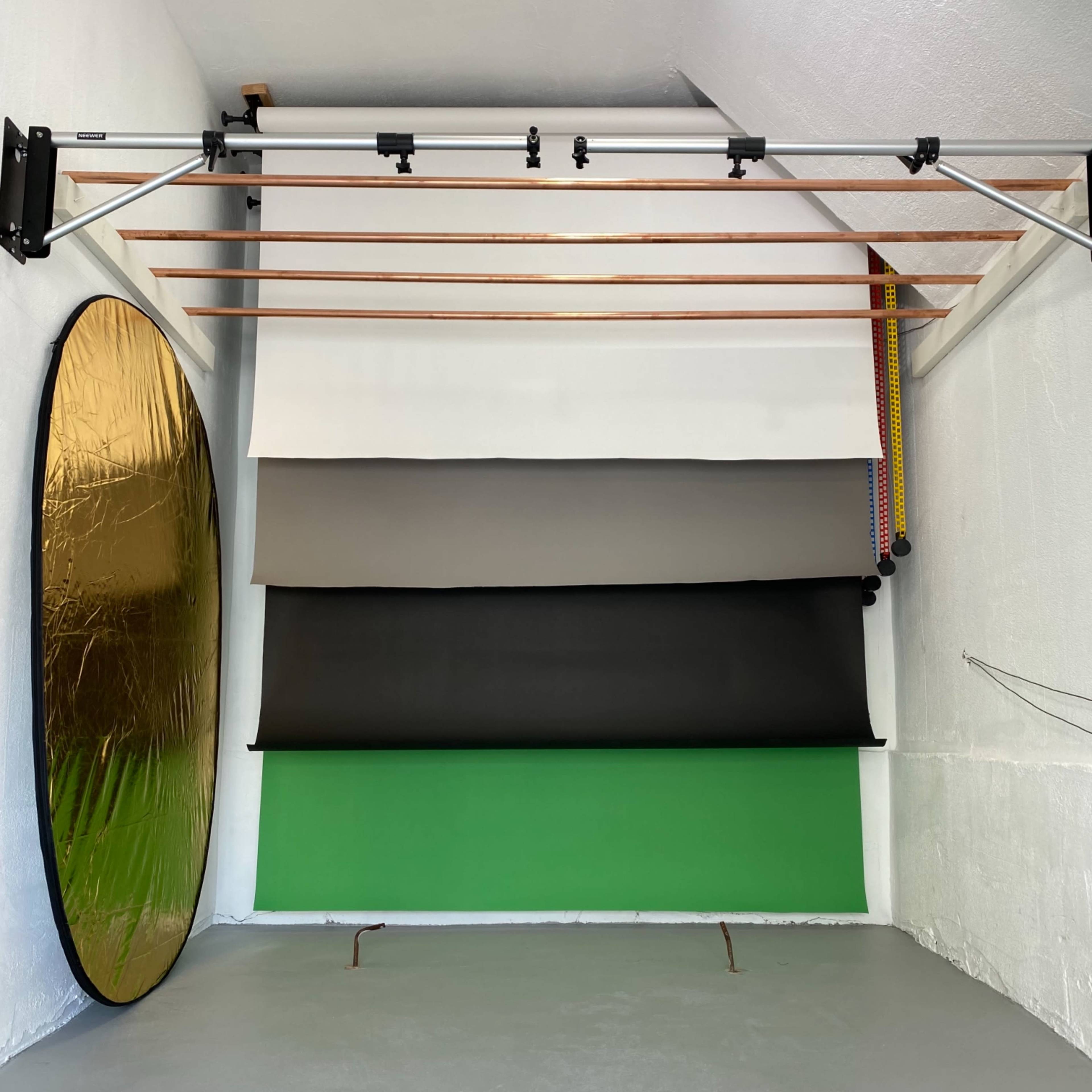 A photography studio with a selection of backdrops, including green, black, gray, and gold, arranged against a white wall.