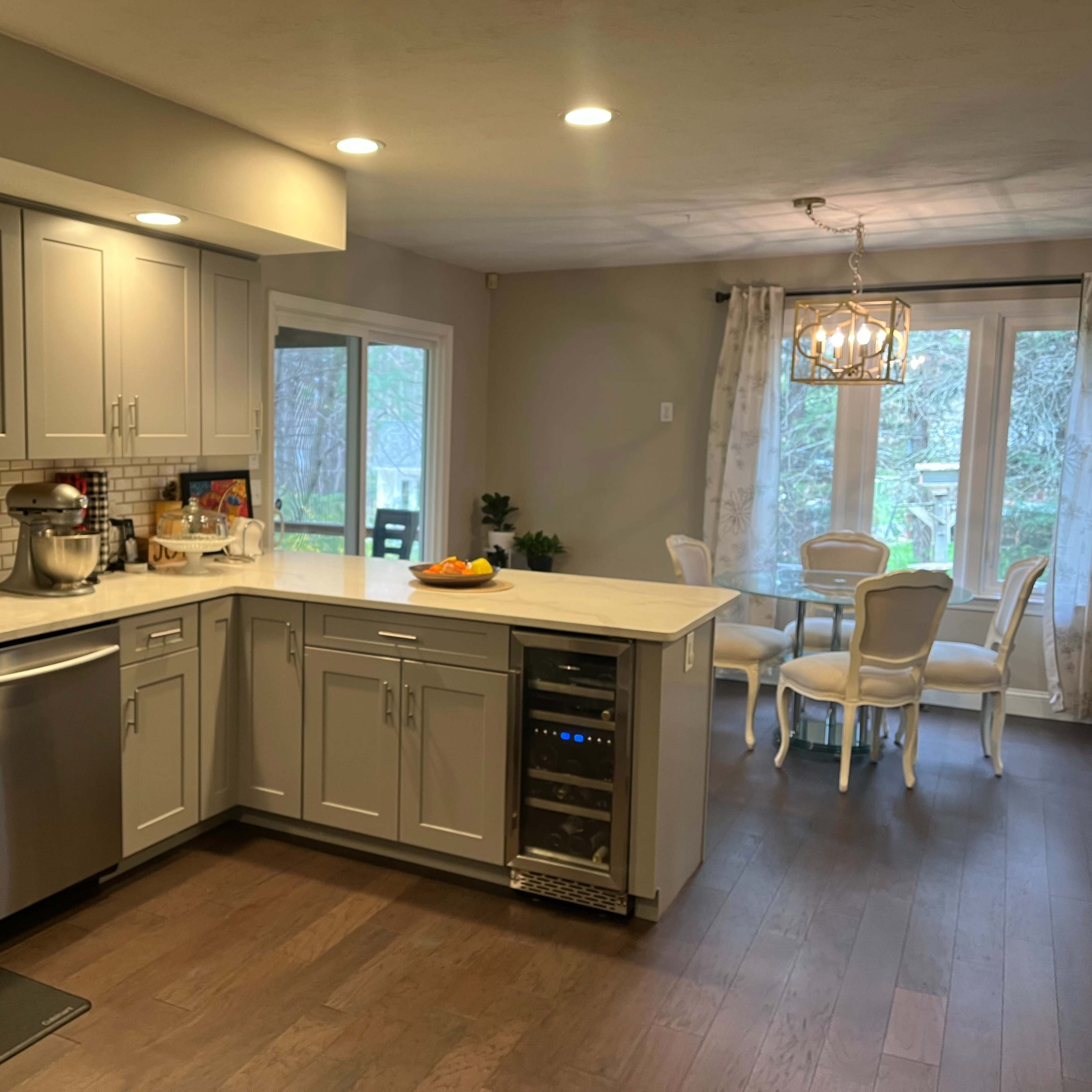 A spacious kitchen with gray cabinets, a stainless steel sink, and a countertop next to a small dining area featuring a round table and chairs.